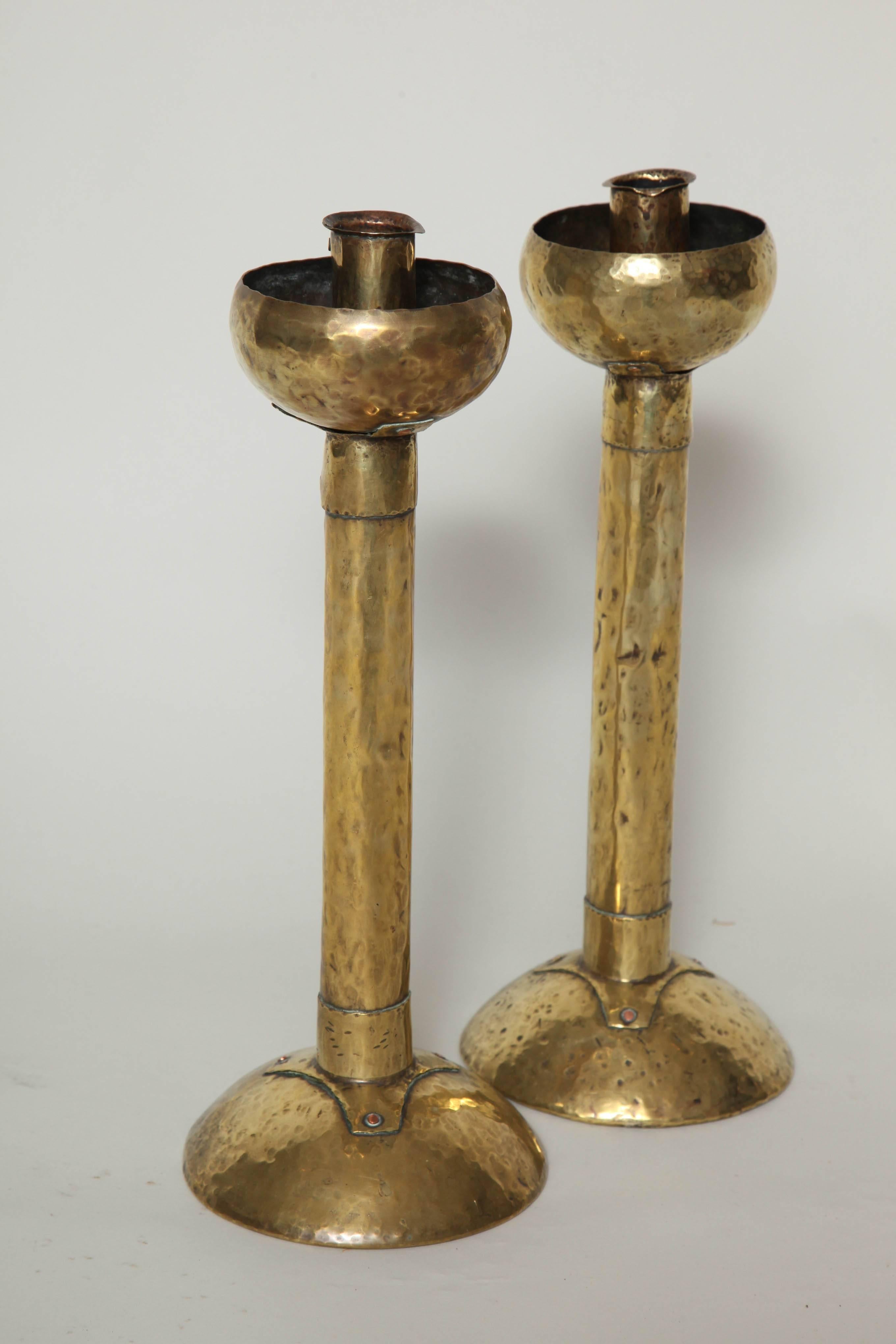Unusual pair of English or Scottish hammered brass candlesticks, the half spherical cups and bases connected by even waisted shafts fastened by hand-hammered rivets, the whole of pleasing design.