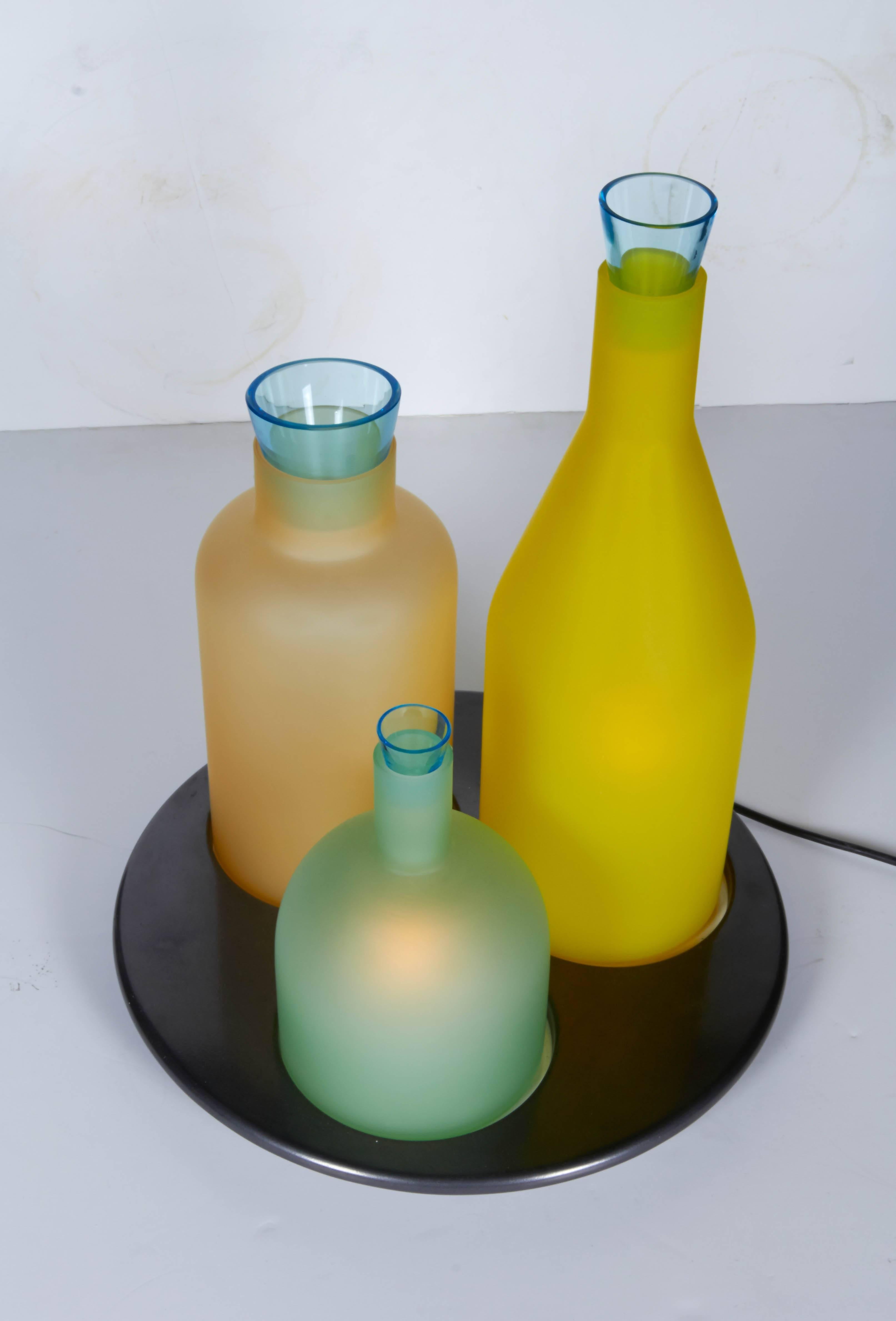Designed by Gido Rasati in the 1980s for extinct lighting company Itre, this table lamp is named Bacco 1-2-3. Each bottle shape shade and top light blue stopper are handblown glass. The bottle shades are satin finished in green, amber and yellow