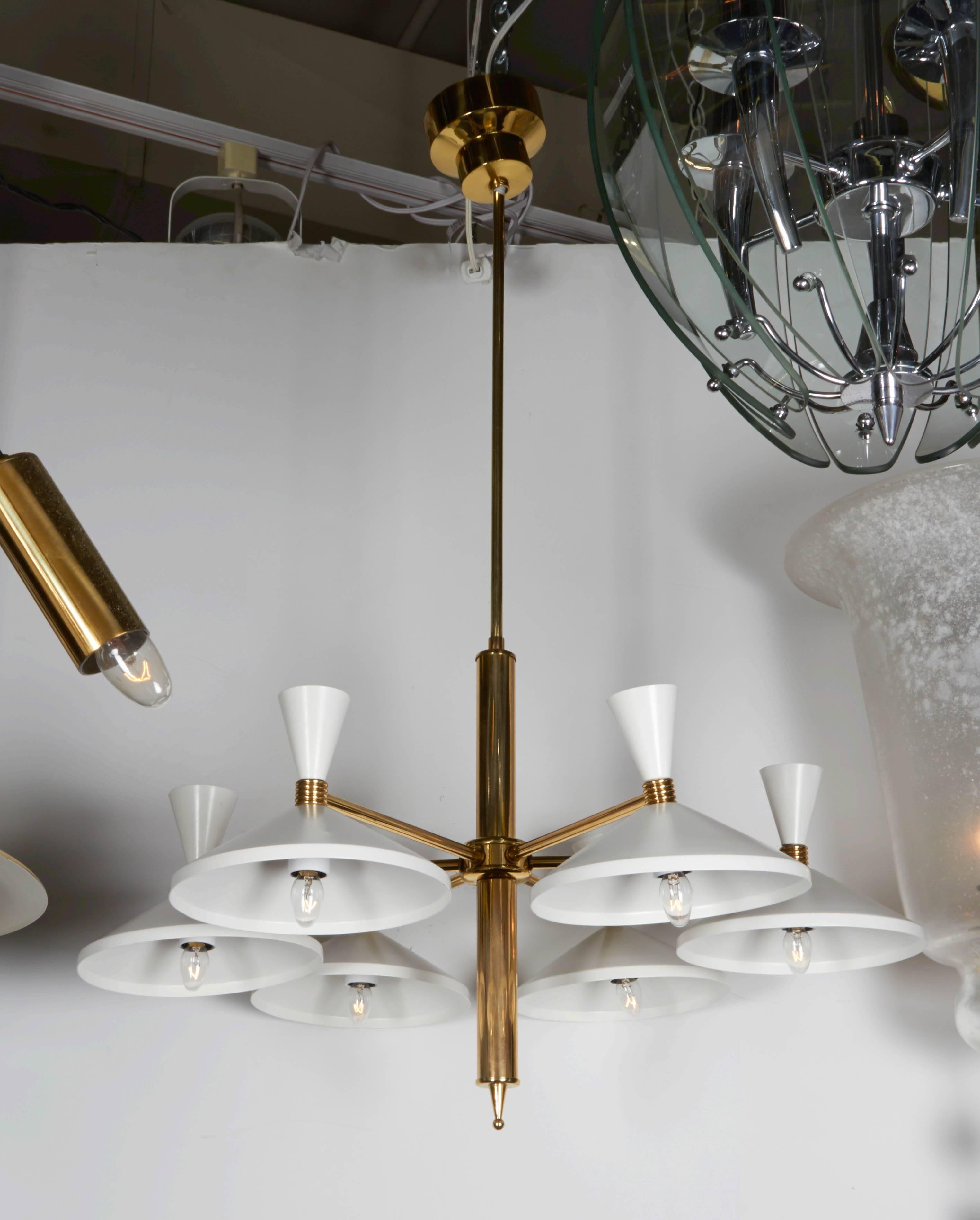 A 1950s modern design brass and white enamel metal six-light chandelier. Each brass arm holds a wide down facing shade with a cone shape decorative top in white enameled metal. Original brass ceiling canopy. Requires six candelabra bulbs. Chandelier