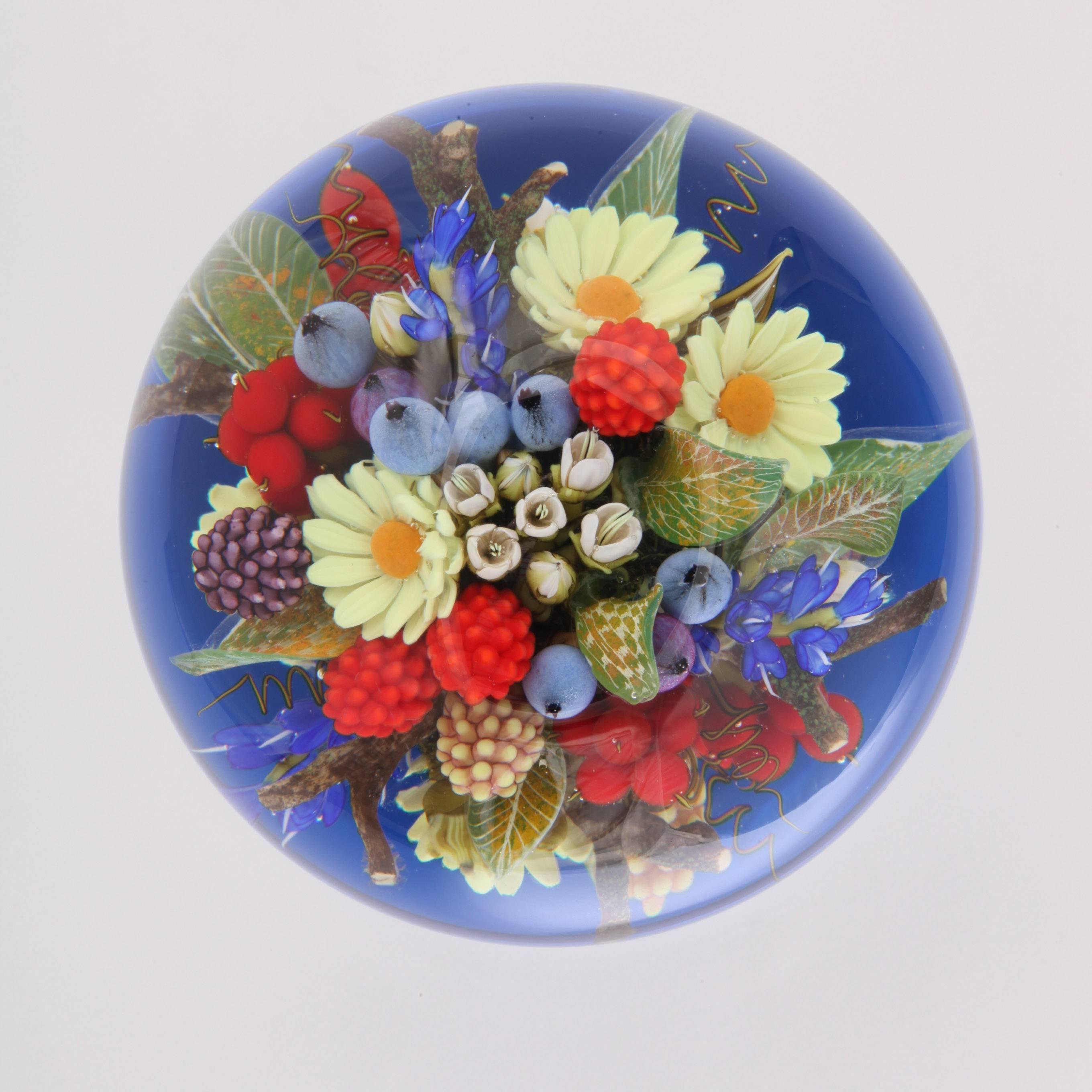 A beautiful David Graeber pedestal paperweight with a compound bouquet of yellow daisies, blue and white flowers and raspberries and blueberries, on a cobalt blue and glass foot.
