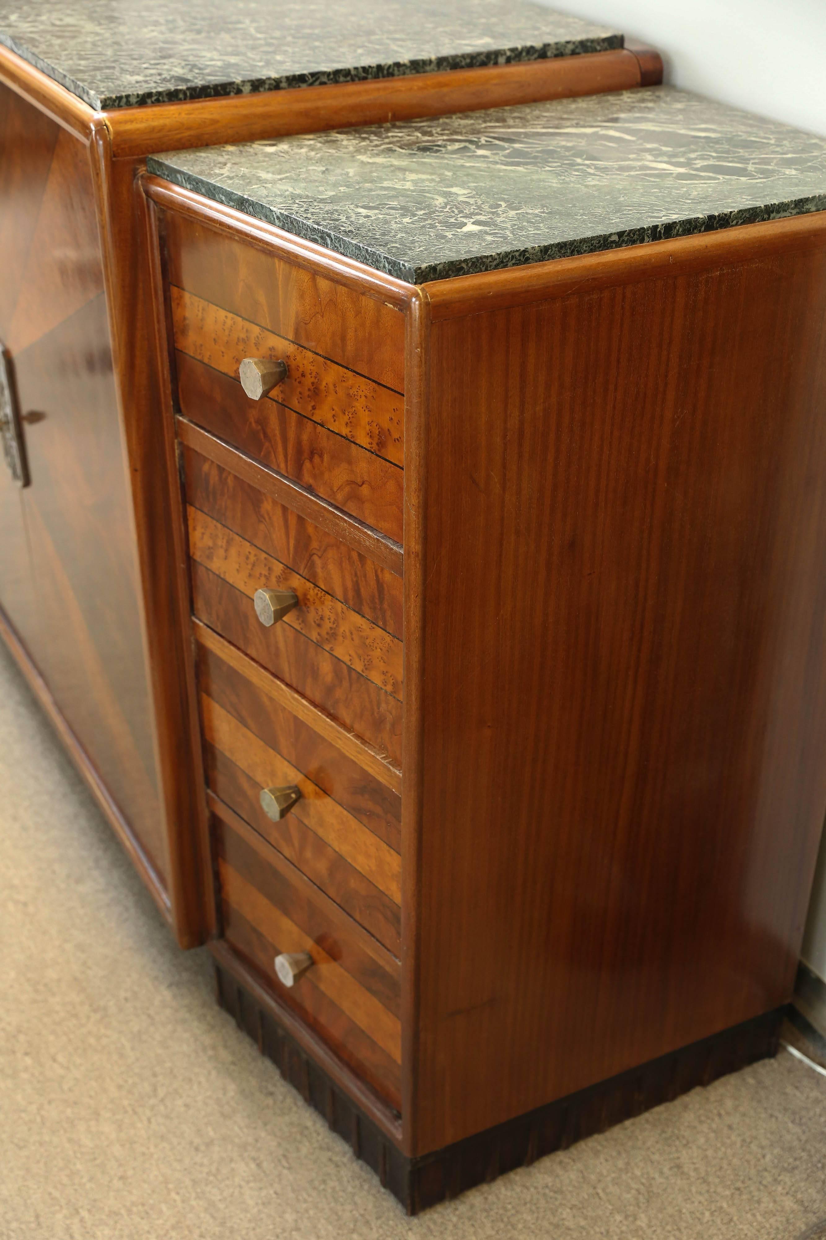 Mahogany, wood veneer decorates this well designed furniture. Having two columns housing four drawers on either side which are holding a suspended middle section that has two large double doors. Original silvered hardware. Marble tops over the