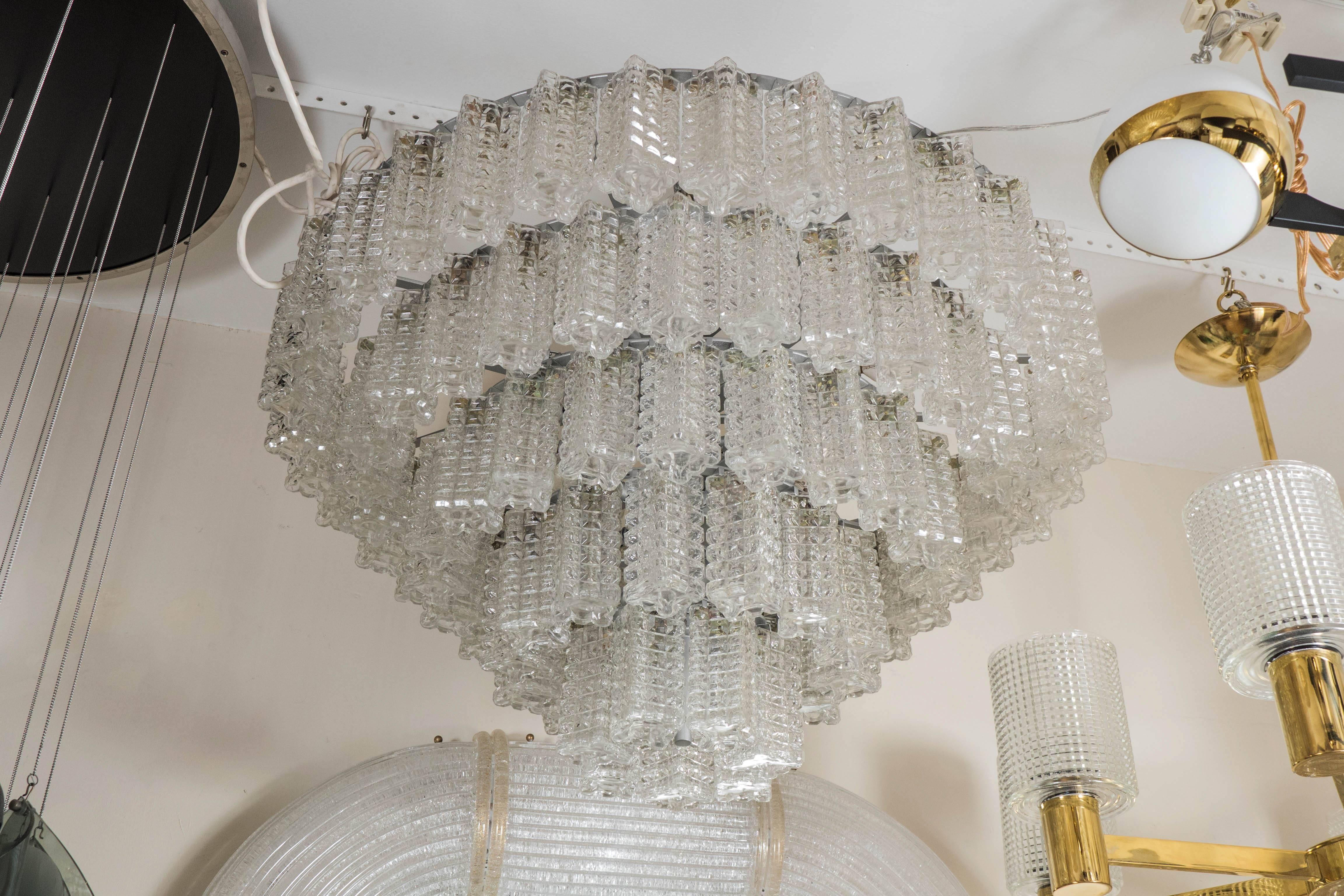 Circular, five-tier chandelier composed of textured glass rectangular elements.