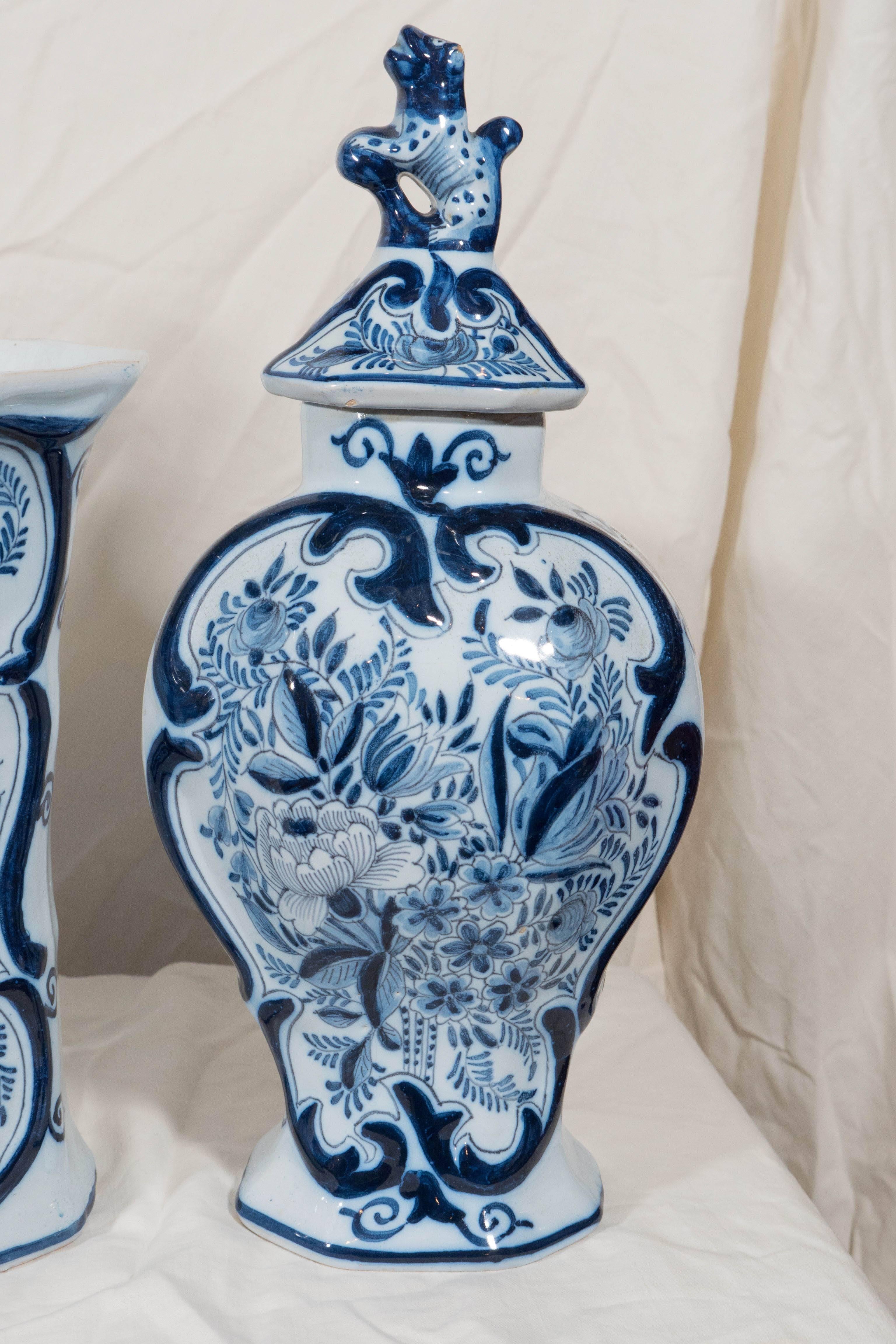 A Dutch Delft five-piece garniture comprising two trumpet vases and three baluster vases decorated in cobalt blue with a profusion of flowers. Each covered vase is topped by a traditional Dog of Fo finial.
 