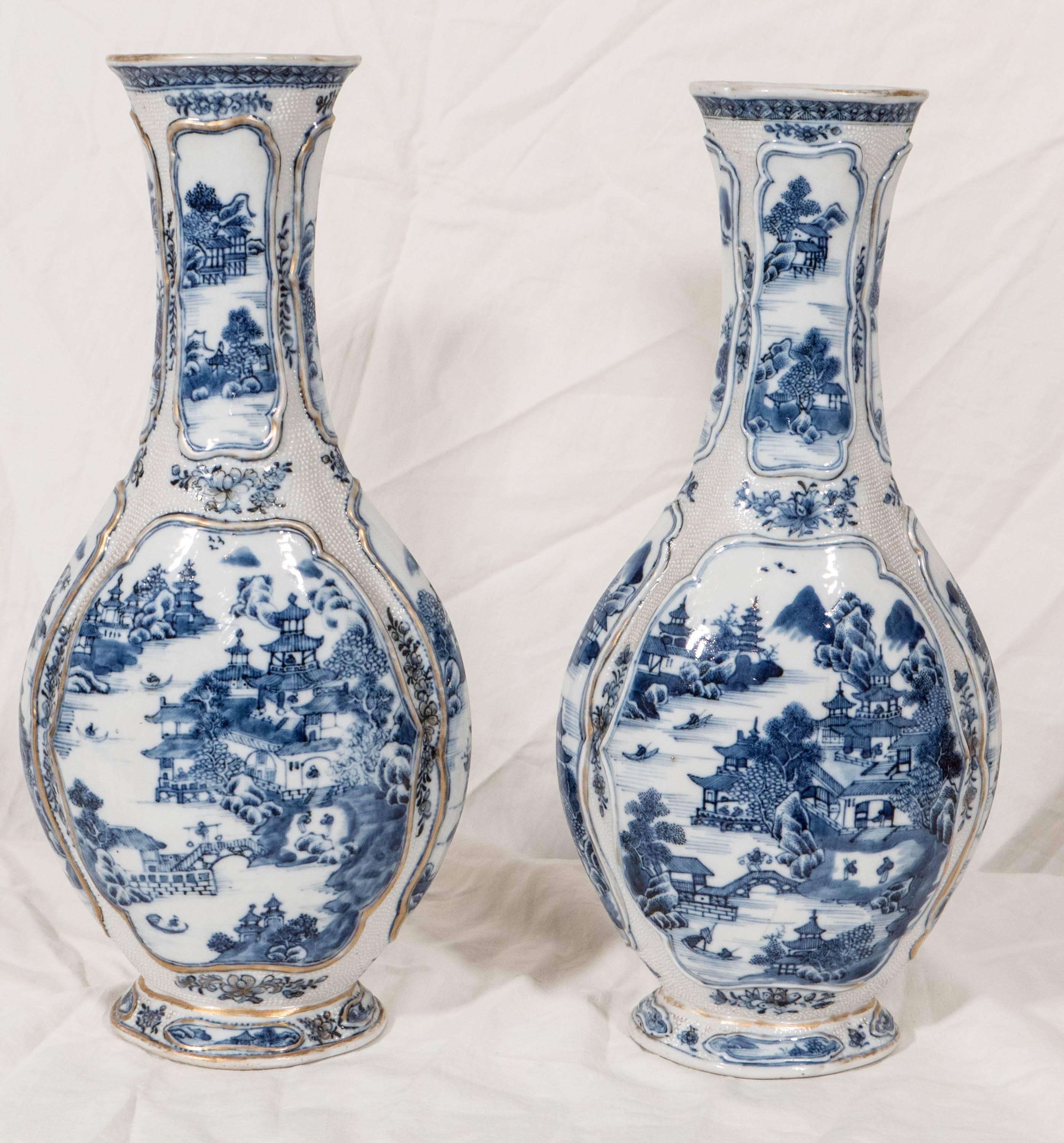 A pair of 18th century Chinese Blue and White flattened baluster shape vases with hand-painted scenes front and back.The decoration features pagodas and waterside scenes. The neck of each vase has smaller elongated panels with similar scenes.