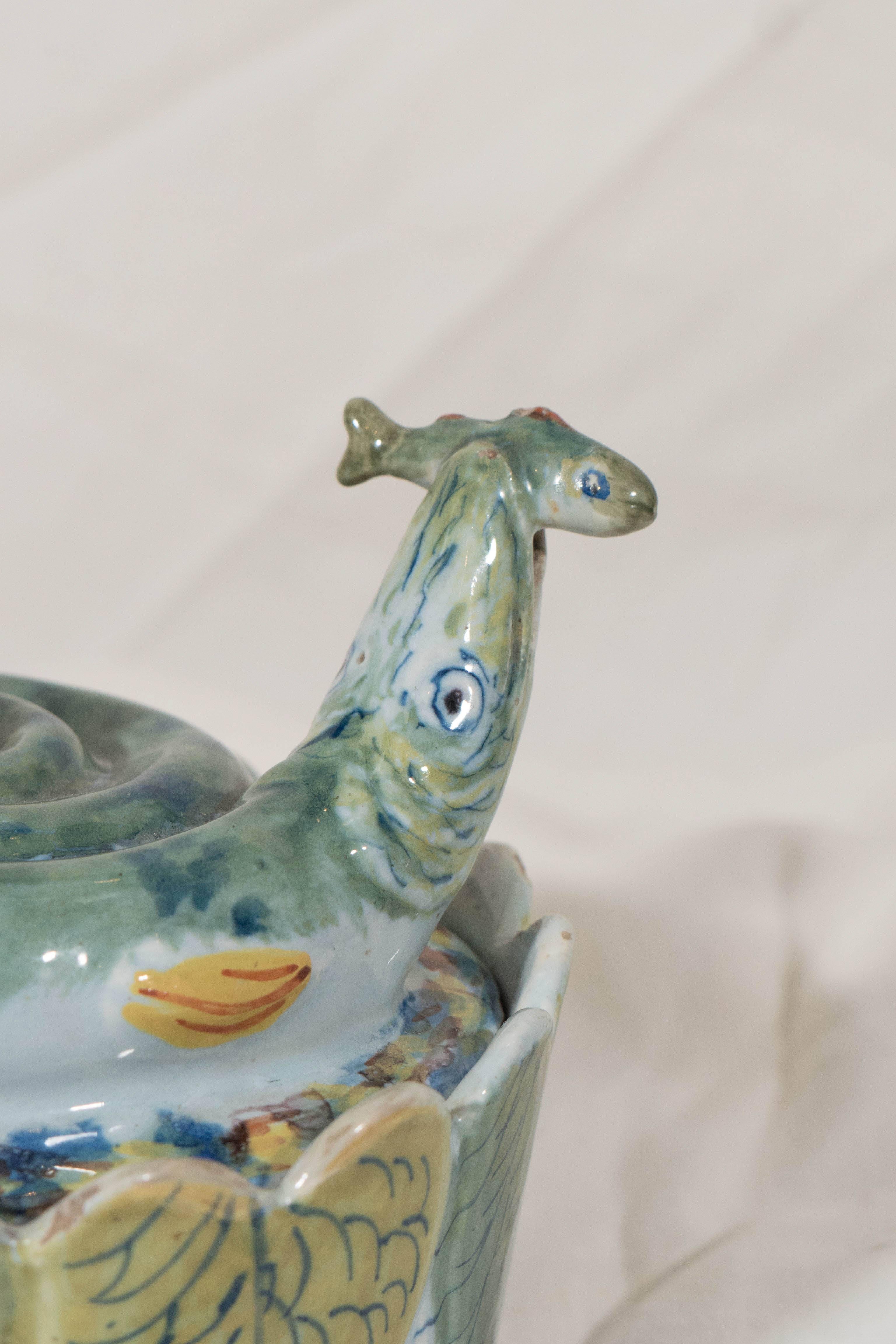 An 18th century Dutch Delft dish and cover painted predominantly in soft greens and blues. The cover is modeled as a curled pike about to swallow a small fish. The pike's raised tail forms the cover's knop. The circular bowl is beautifully molded