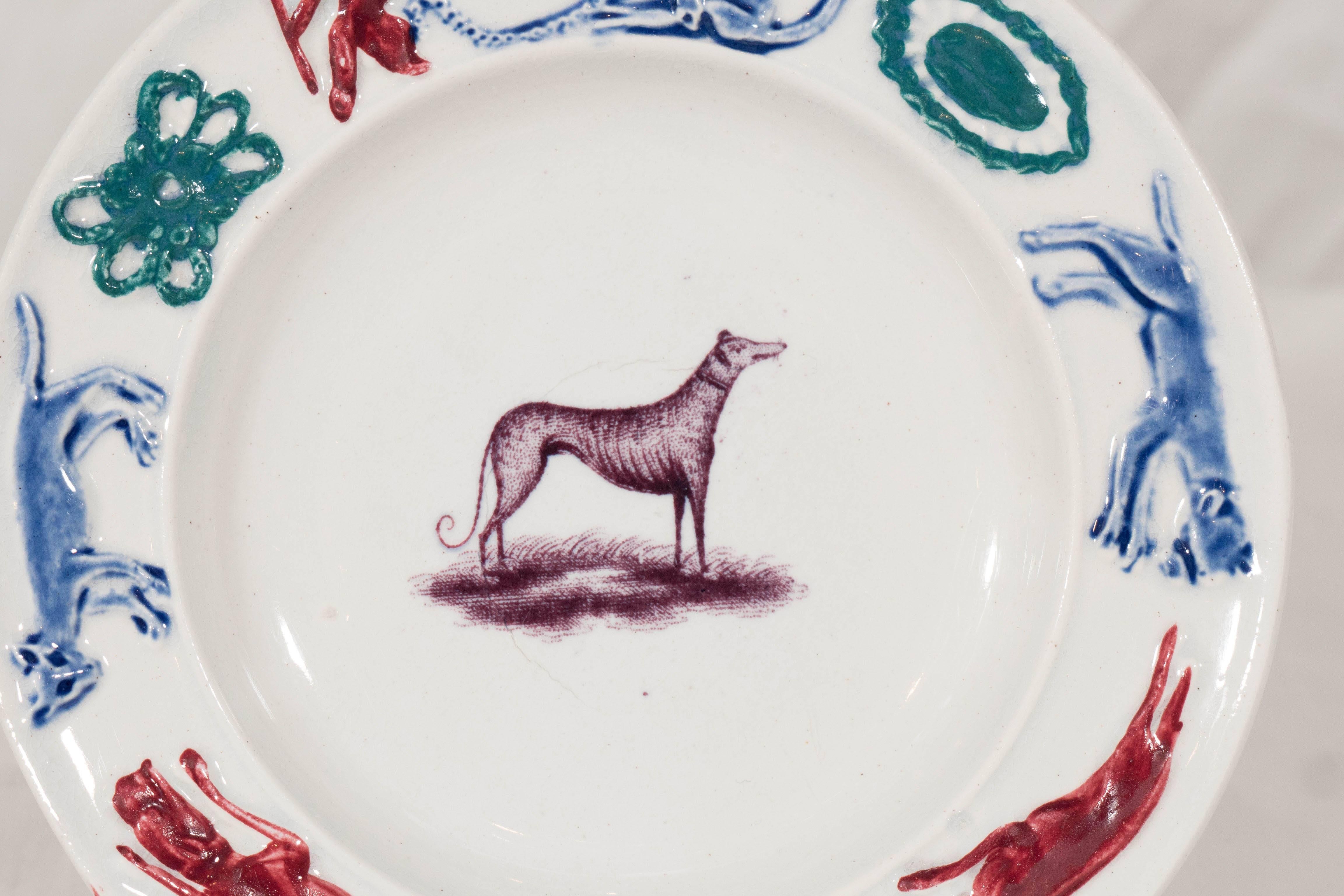Children and dogs are a natural combination. This wonderful Adams child's plate shows a greyhound in the center around which are colorful figures and decorations including: a blue monkey and his red trainer, a  blue raccoon, and a red fox.
