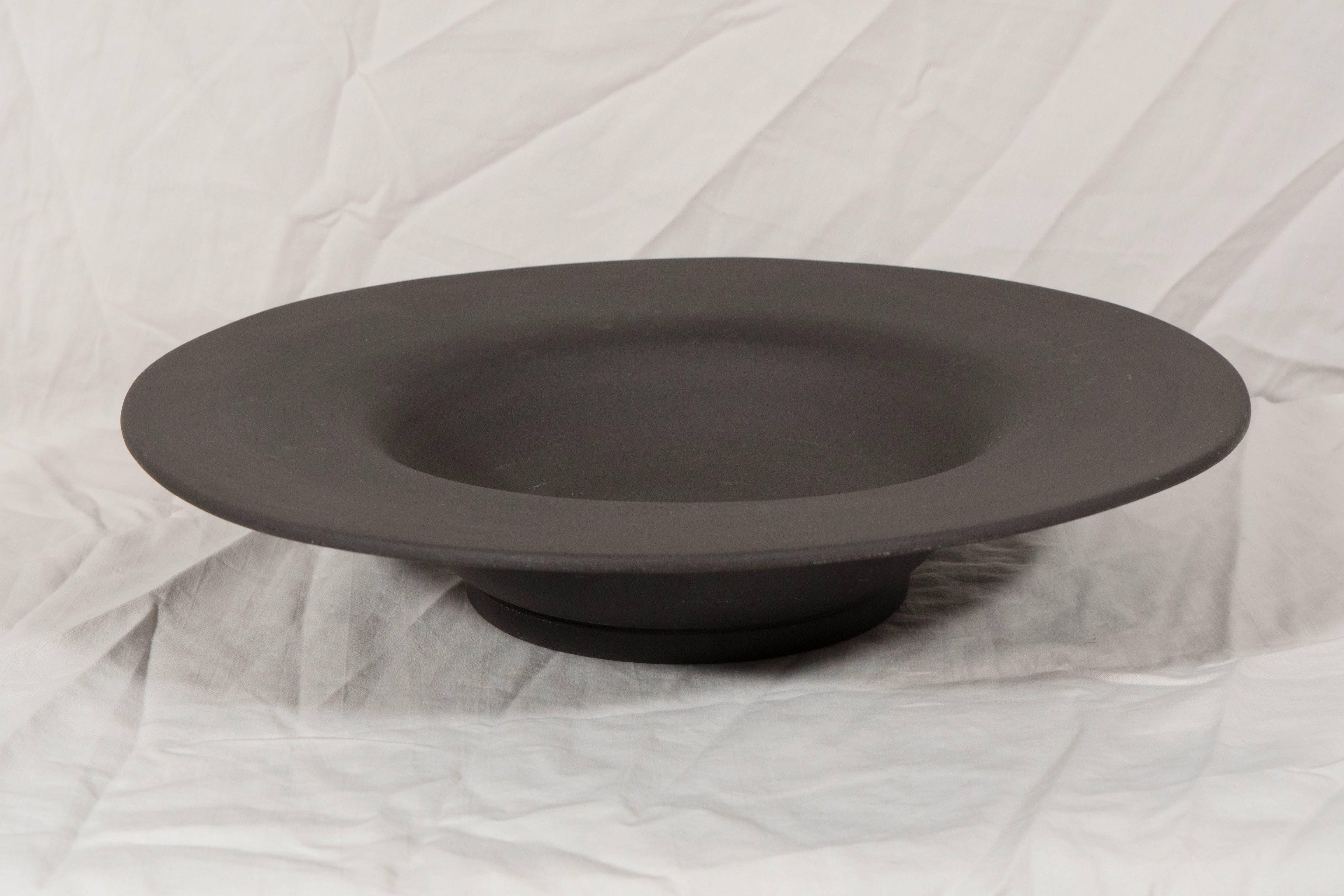 A Wedgwood black basalt bowl in a simple open form with a wide lip. 
 Black basalt was created by Josiah Wedgwood in the 18th century. Wedgwood transformed Egyptian black, a traditional Staffordshire stoneware, into black basalt. Before Wedgwood’s