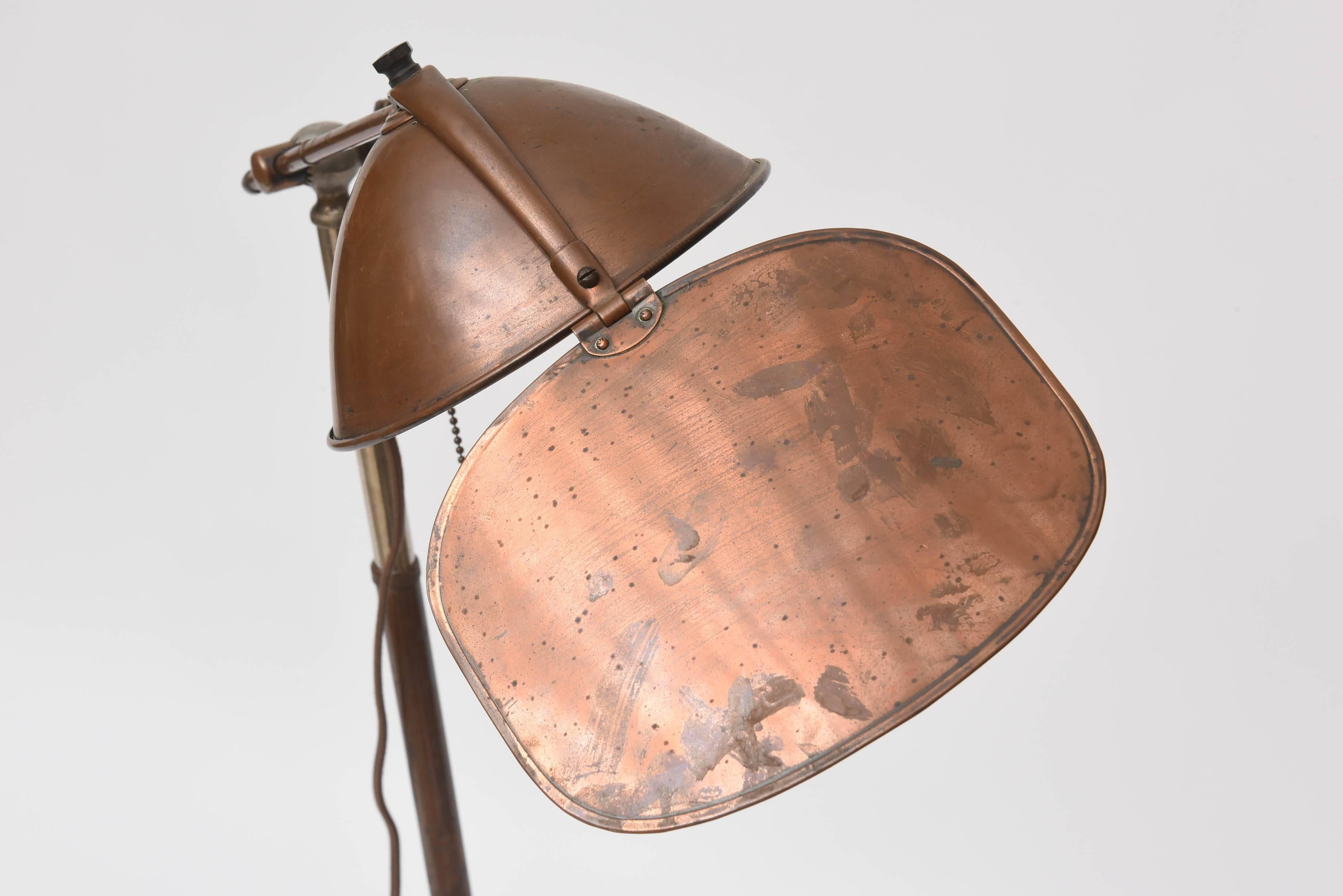 Early 1900s copper medical floor lamp by Lyhne Lamp Company. Visor moves up and down and side to side to diffuse the light. Height adjusts from 34