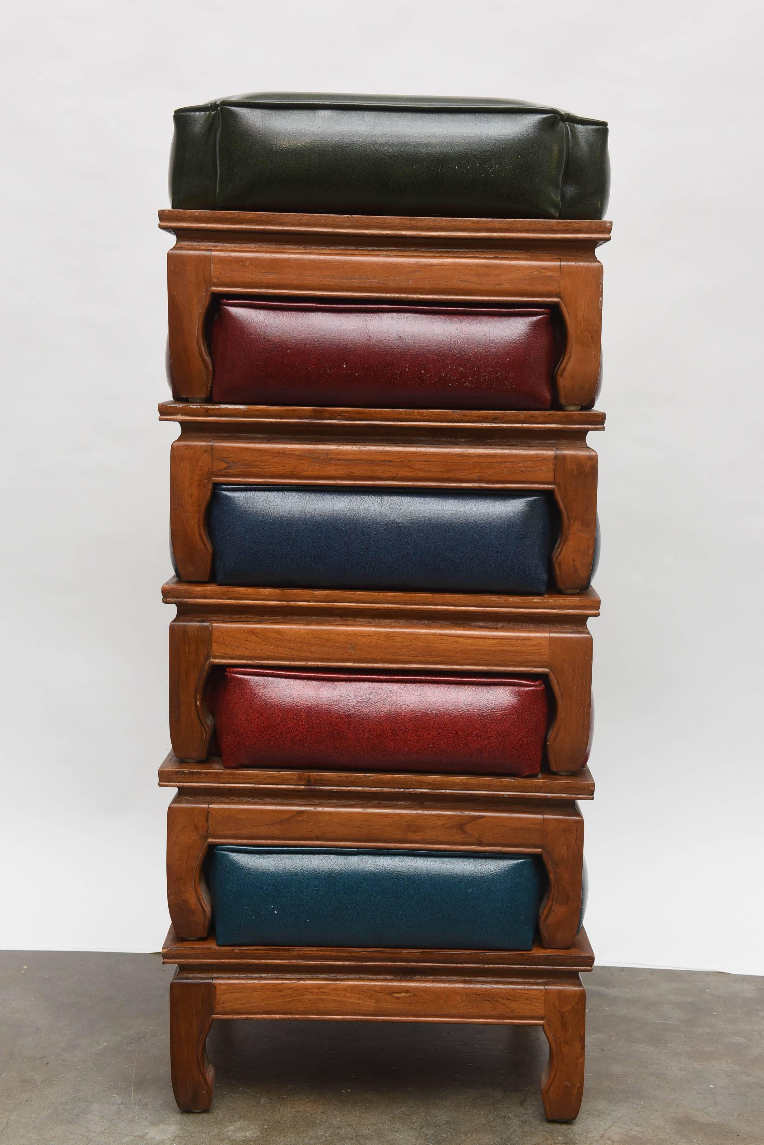 Unusual and practical set of five stools/ottomans that stack on top of each other. In alternating naugahyde colors of red, blue and green with wood bases. Each individual ottoman is 11