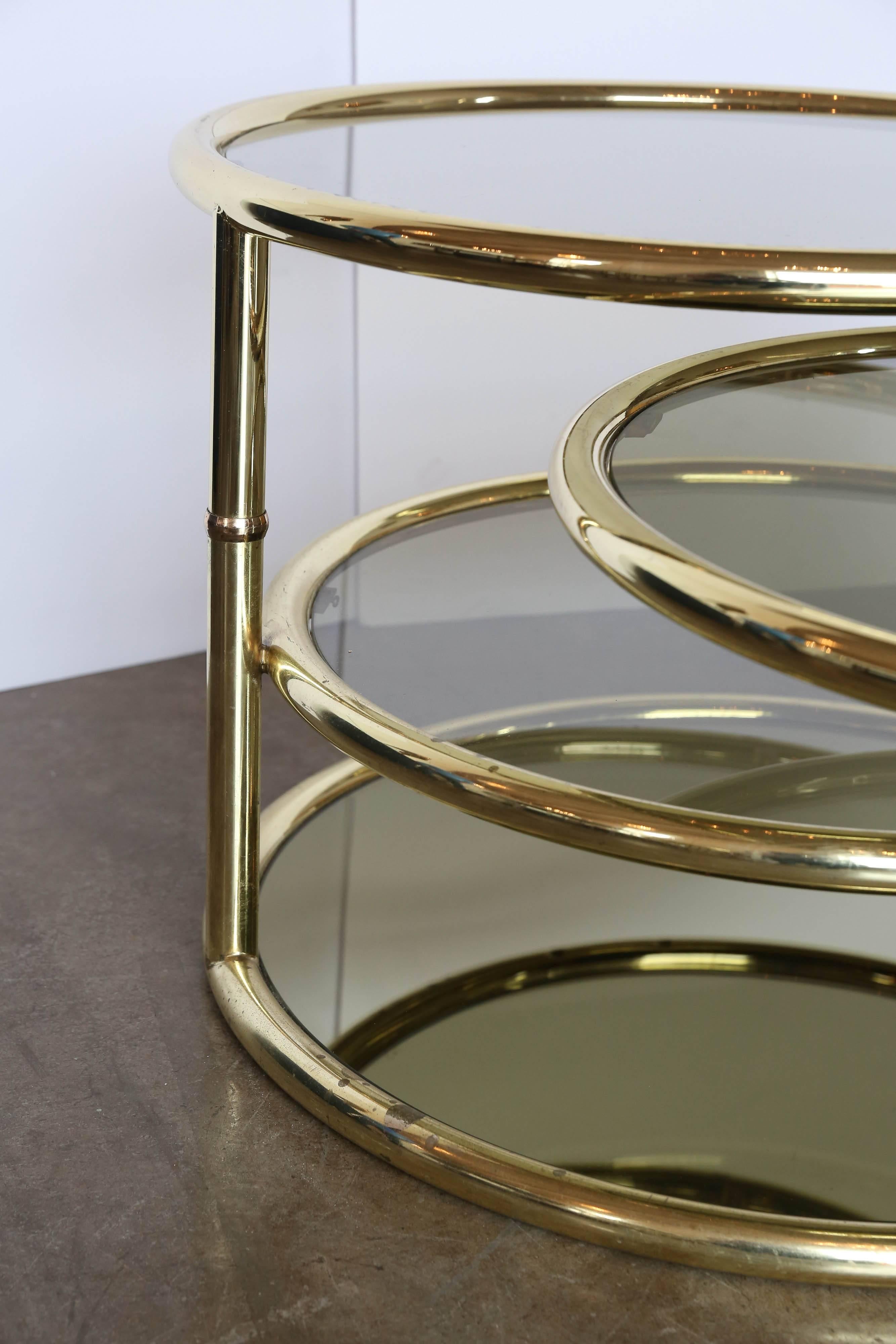 This iconic brass and smoke glass four tier swivel cocktail / coffee / side table is uniquely designed for a great modern look with utilitarian use.  The piece offers four tiers that can swivel out for entertaining or fold in for a tighter fit.  The