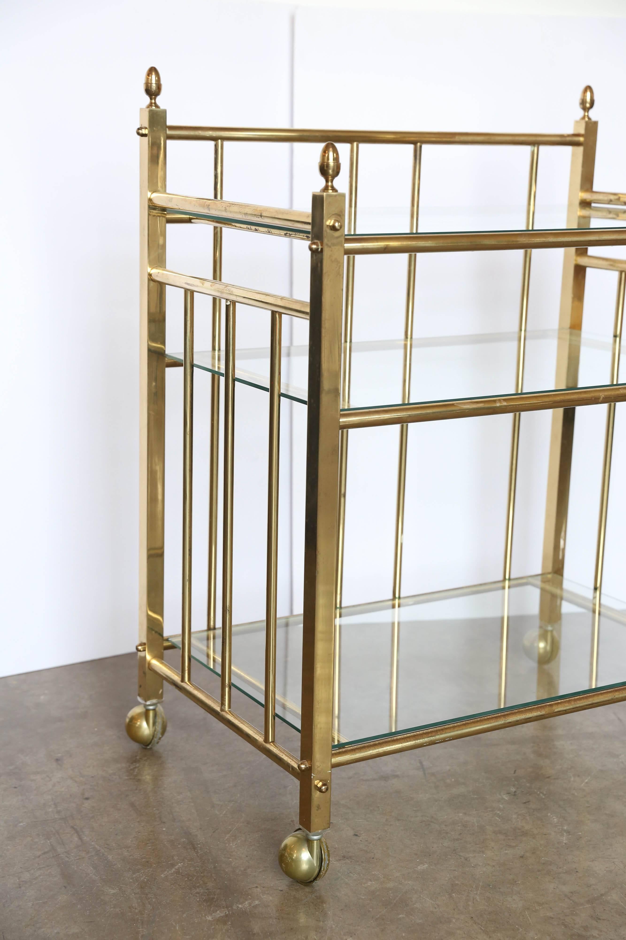 Offered is a Classic regency style brass and three tier glass bar cart with decorative acorn brass finials and brass rollers. This piece is as good looking as it is versatile and would compliment any space.