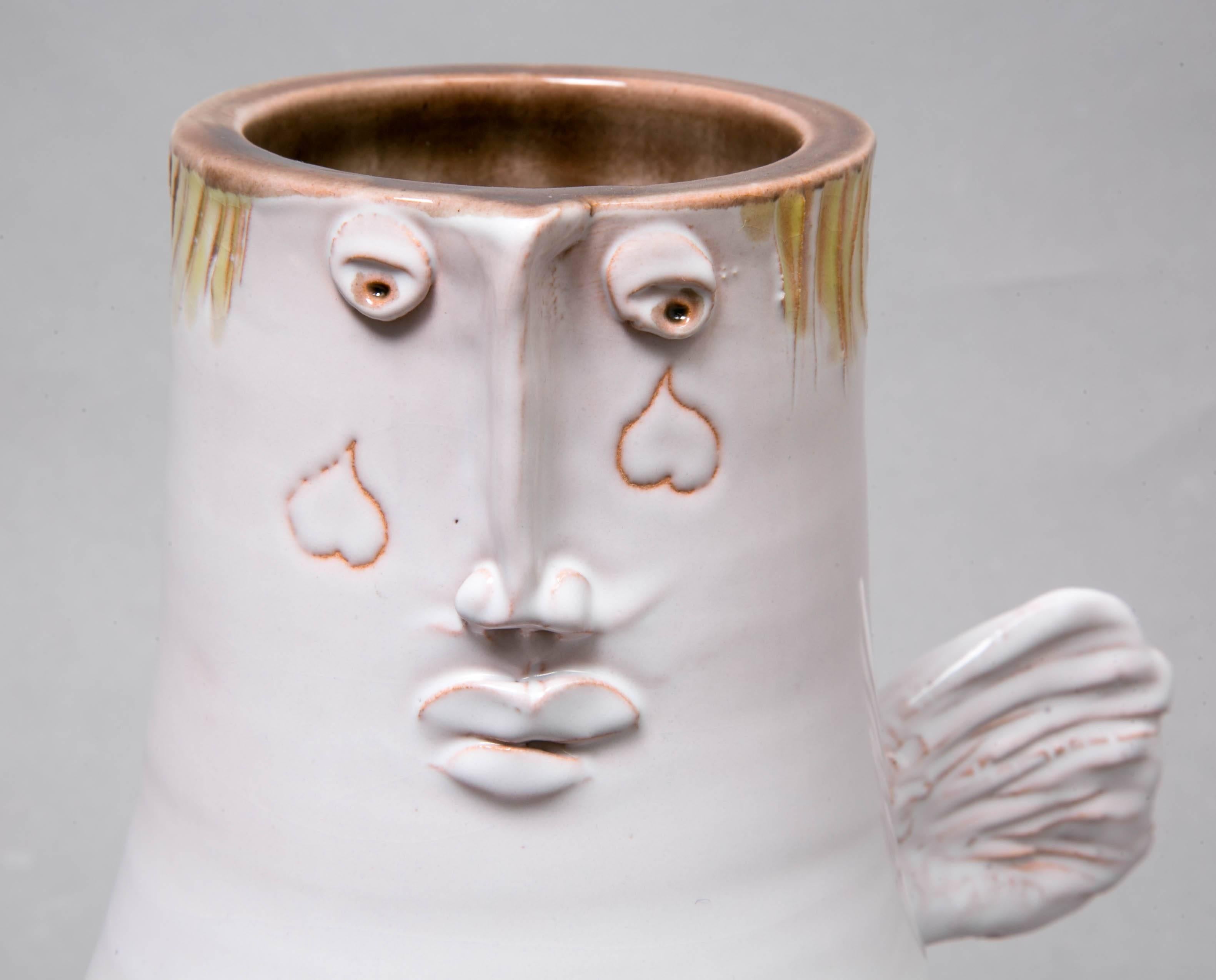 White winged vase with a face, circa 1965, by Robert et Jean Cloutier, France (1930-) / (1930-2008).
White enamelled earthenware with relief. 
Signed Cloutier. 
Ref.Cloutier: P.Favardin Les Cloutier, Paris, 2014, Autre vase Ange p.87.

