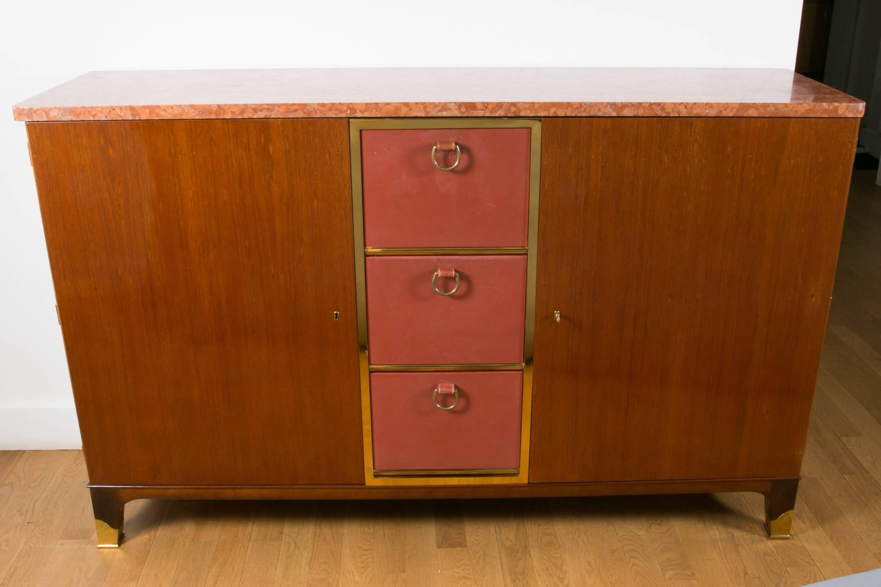 Important mahogany and red leather sideboard cabinet, 1958, by Paul Dupré-Lafon, France (1900-1971).
Opening with three central flaps and with two doors on Inside with two drawers and shelf. Gilt brass central frame, red marble top, gilt bronze