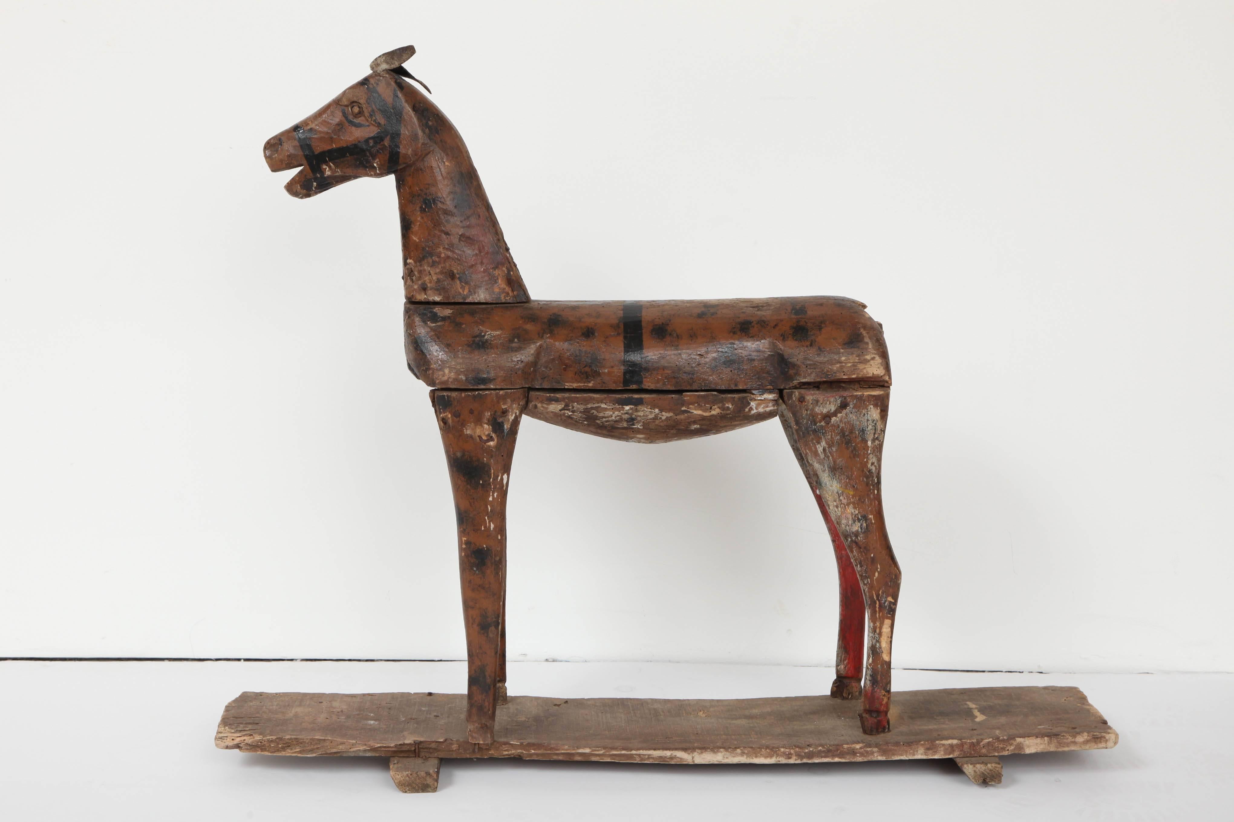 A French carved and painted wooden toy horse, late 18th century, of naive form with dappled paint and leather ears, set on a wooden base which may have had wheels at some point.