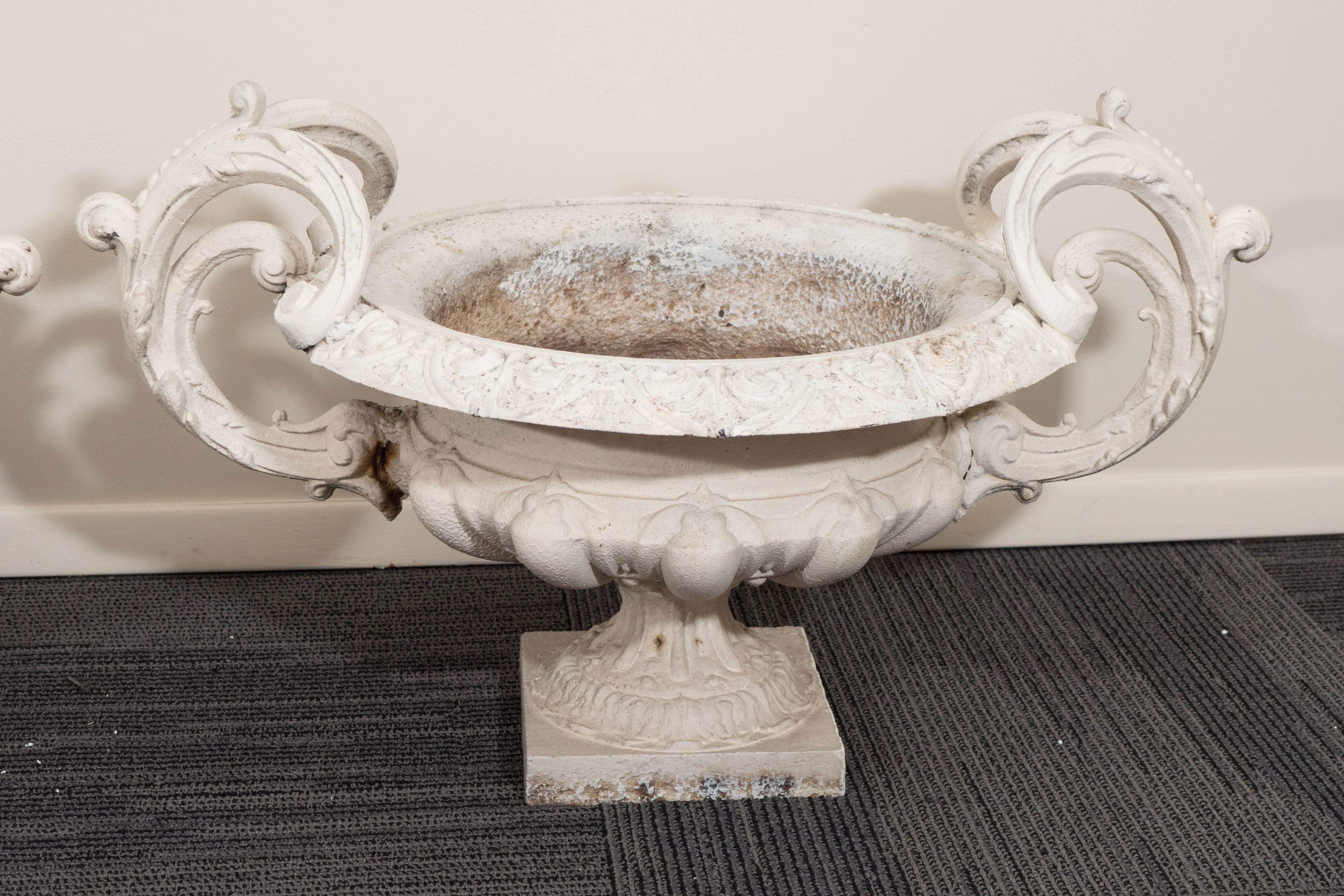 A pair of vintage, cast iron urns, produced within the early 20th century period, circa 1900-1910, each painted in white, with classical patterned detail to the rim, over a gadrooned body, flanked with scrolling acanthus handles. Other than age