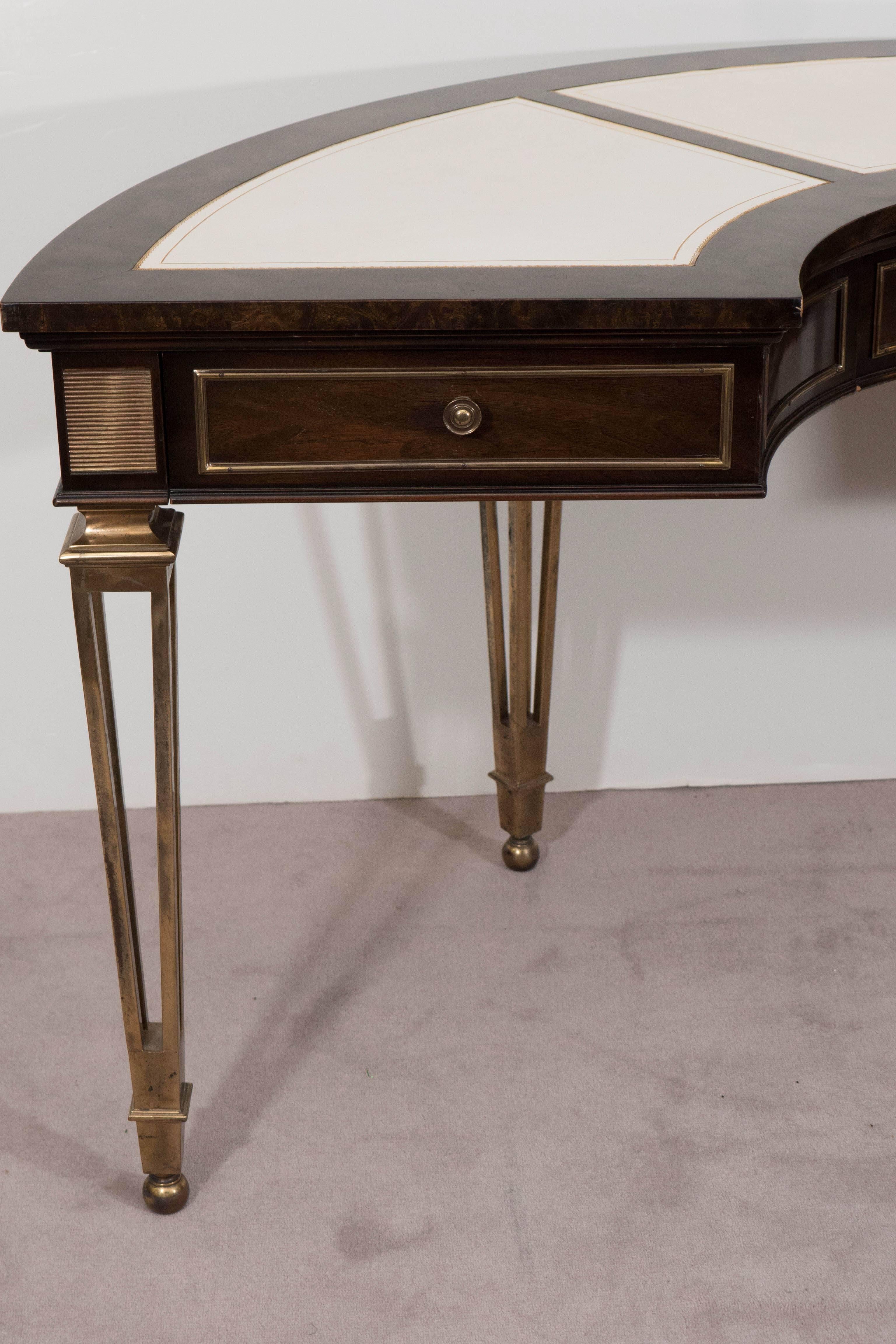 A vintage demilune desk, produced by Mastercraft, circa 1960s-1970s, designed in the refined neoclassical mode, veneered in burl wood and inlaid with three sections of white leather tops (with finely detailed gold borders), including five drawers,