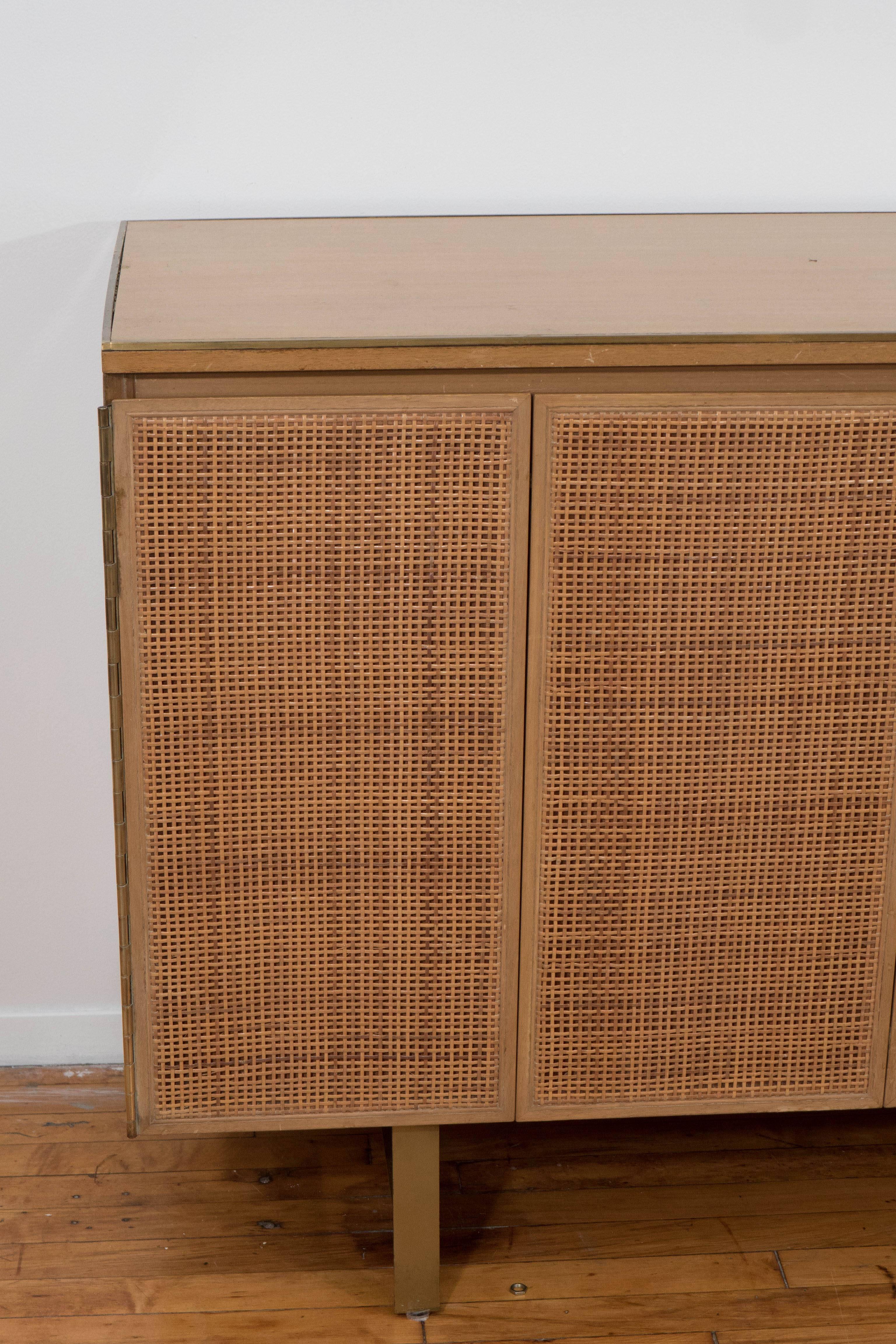 A vintage, circa 1950s wooden credenza on raised brass, designed by Paul McCobb for Calvin Furniture Co., including two three-panel doors, each with caning to the front, which open to reveal two drawers, above separated storage spaces. Markings