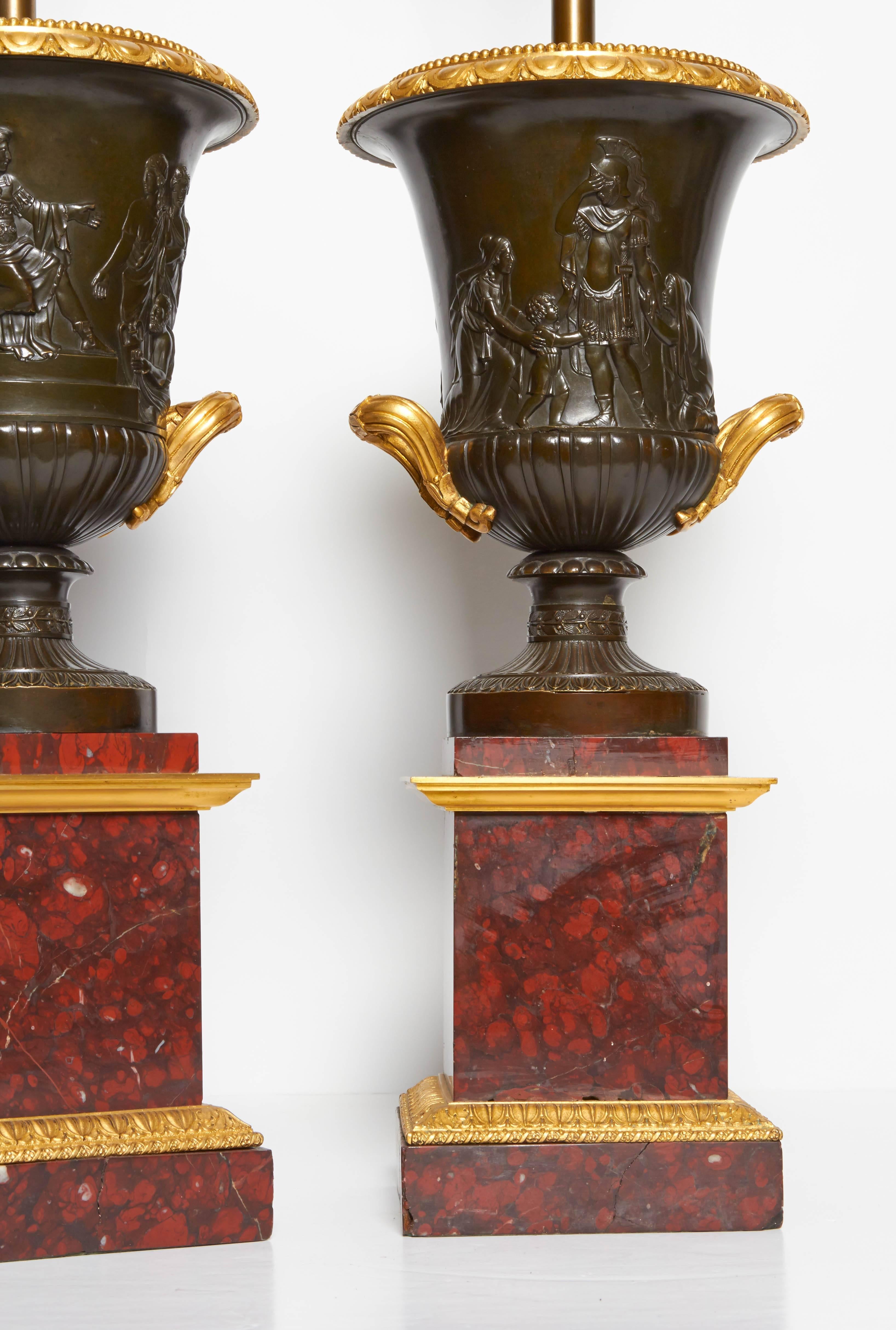A fine pair of antique neoclassical grand tour period, two-toned patinated and doré bronze, Campagna shaped two handled urns. Each beautifully resting on an original rouge marble plinth finely mounted with ormolu mounts. Each vase finely casted and