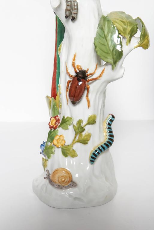 A fine pair of antique Meissen porcelain figures of colorful parrots, each standing on a tree branch. One having cherries and strawberries and the other parrot bearing flowers and Insects including a snail, and a silk worm crawling up from the
