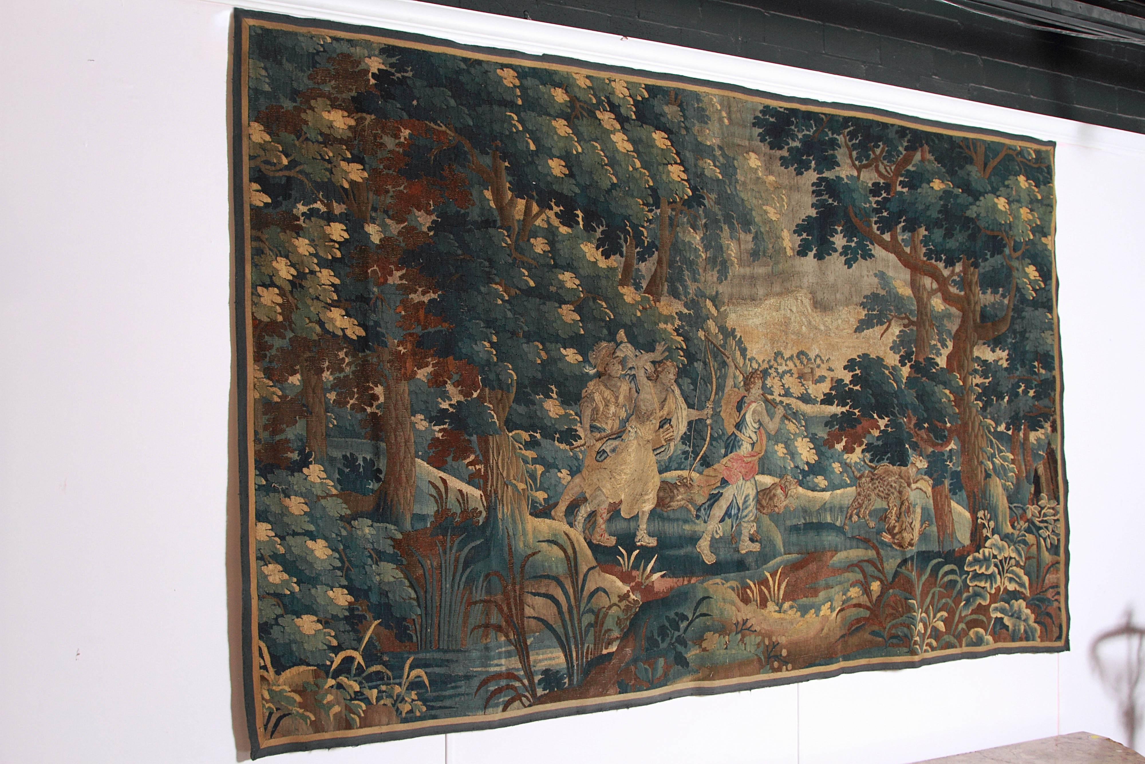 This superb wool and silk Aubusson tapestry depicts Diana the Huntress with two attendants on a wolf hunt in a forest. One attendant is a falconer holding his falcon and the other holds a spear. There are hunting dogs at the center, one of which has