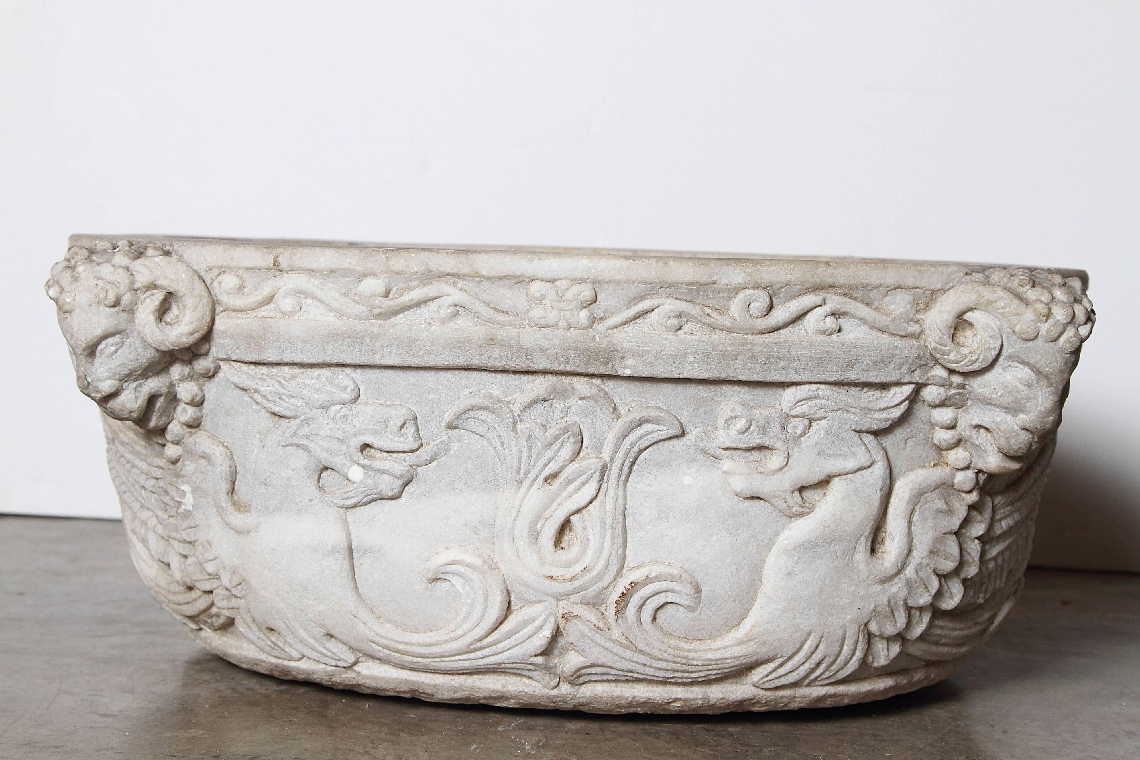 This elegant antique Italian white marble holy water vessel dates to the late 1700’s or early 1800’s. It has been carved out of one entire large piece of stone.  The marble has beautifully carved motifs depicting a mascaron with ram’s horns, a
