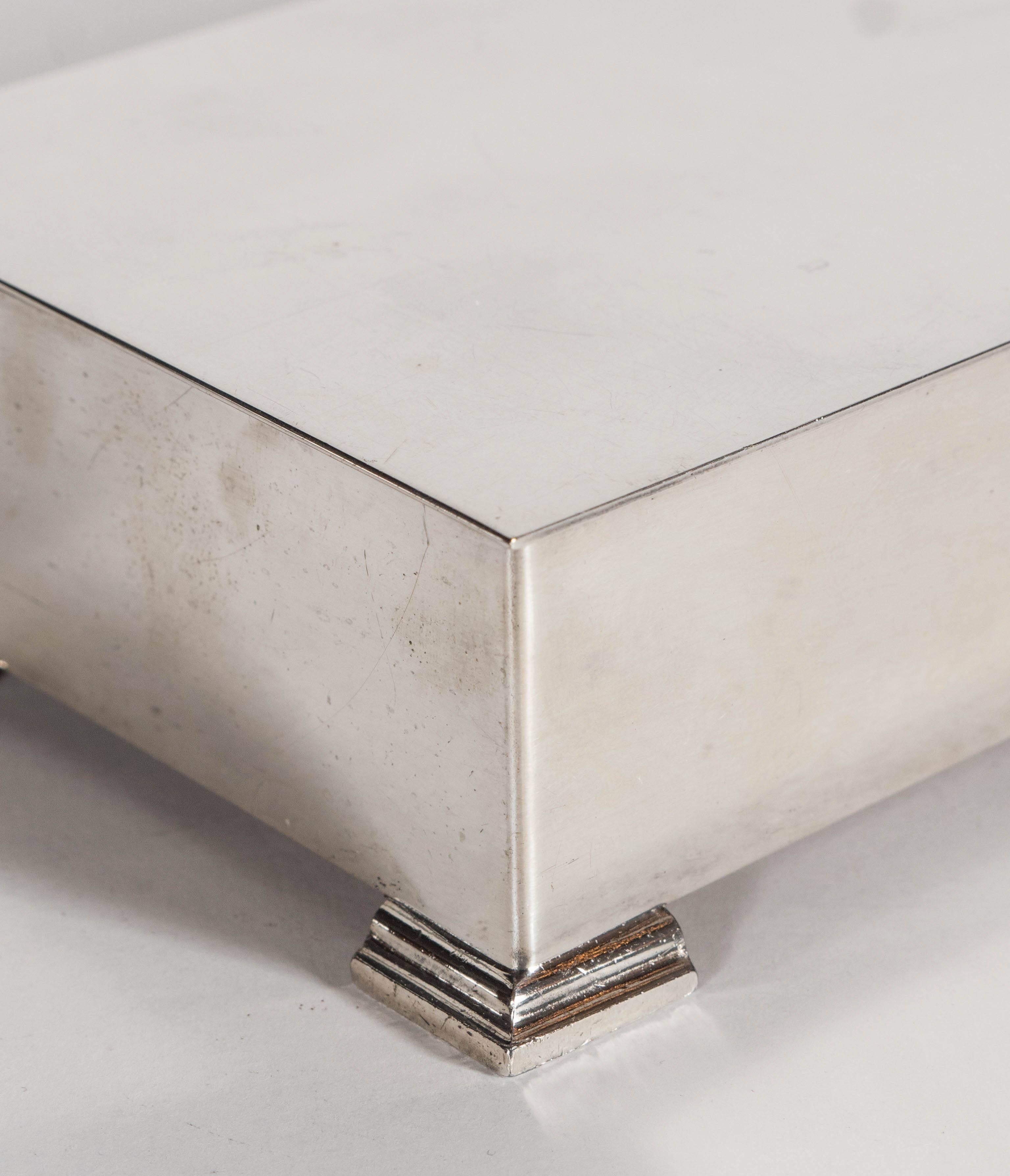 A very elegant art deco silver plated box with four skyscraper-style slightly protruding feet and a flat, hinged top. The interior is lined with thin cedar planks and a divider. A perfect piece to store jewelry, playing cards, keys or smaller
