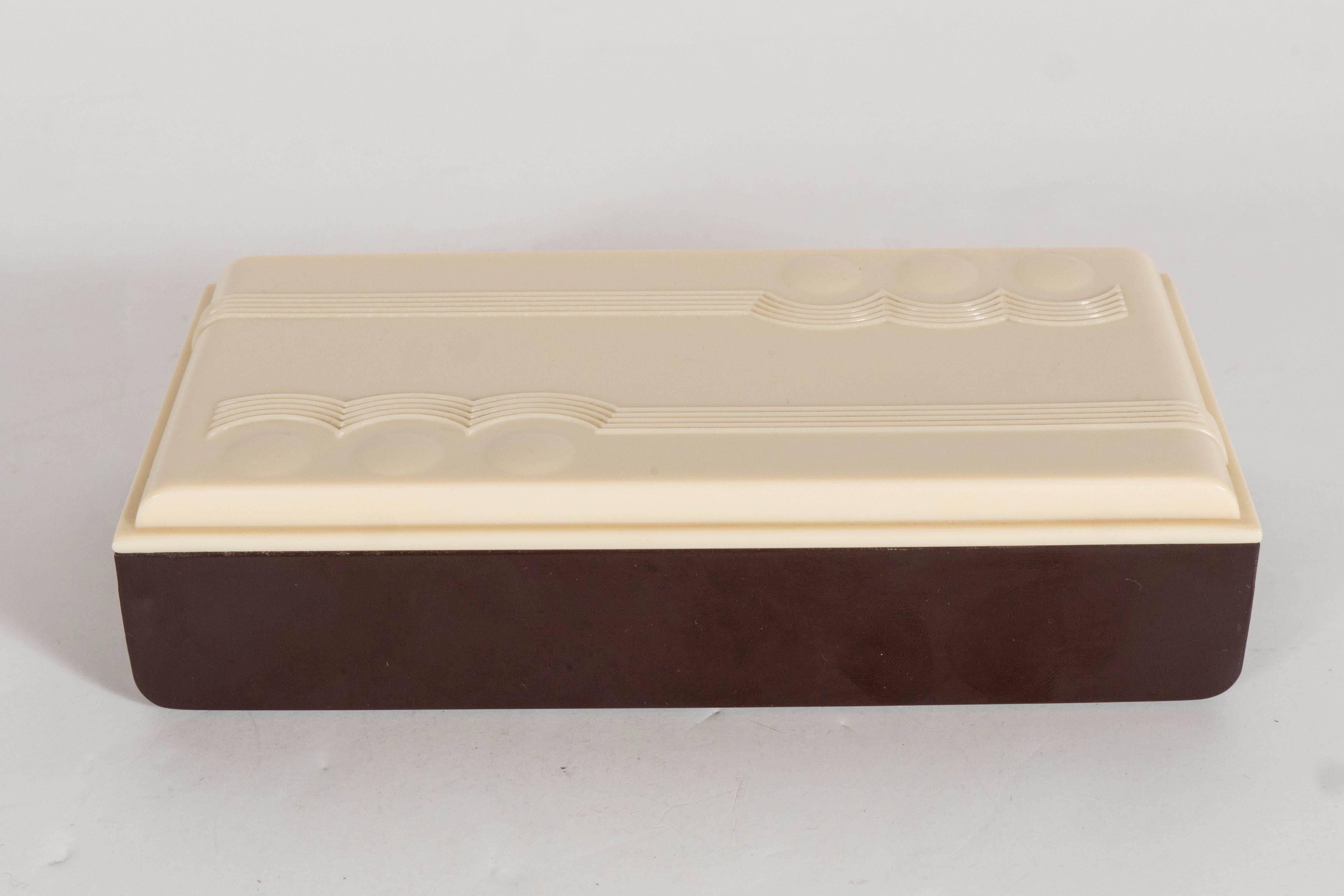 A lovely piece of American Art Deco. A cognac brown bakelite box and ivory-colored lid is adorned with typical deco detailing along its top and down its sides. An excellent addition to any deco lover's collection. Can hold jewelry, keys, cards or