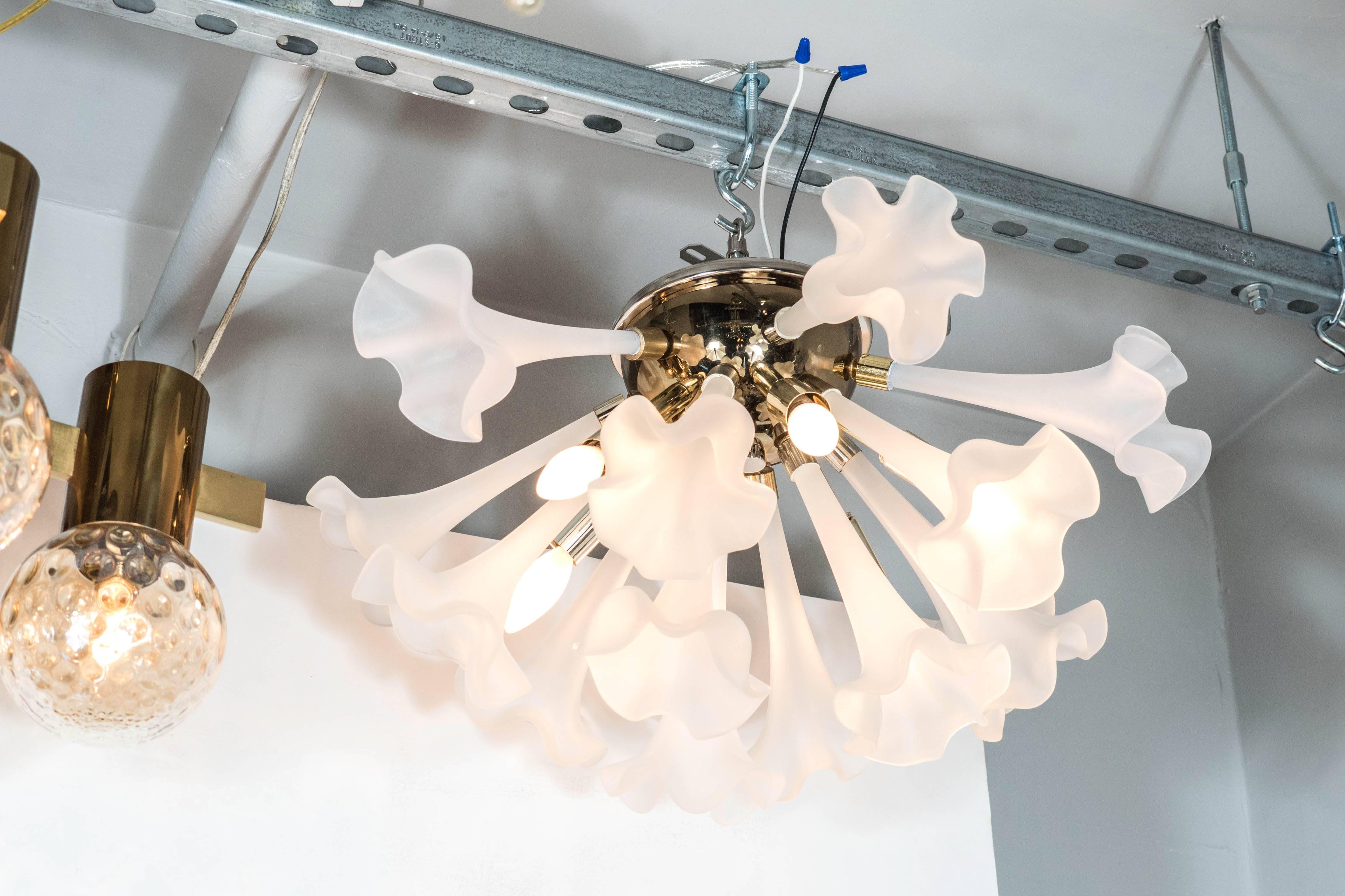 A Mid-Century Modernist flush mount chandelier featuring 15 handblown frosted glass flowers with elongated stems, which attach to a brass base cap. This fixture also holds five candelabra-style bulbs. The frosted glass displays a soft glowing effect