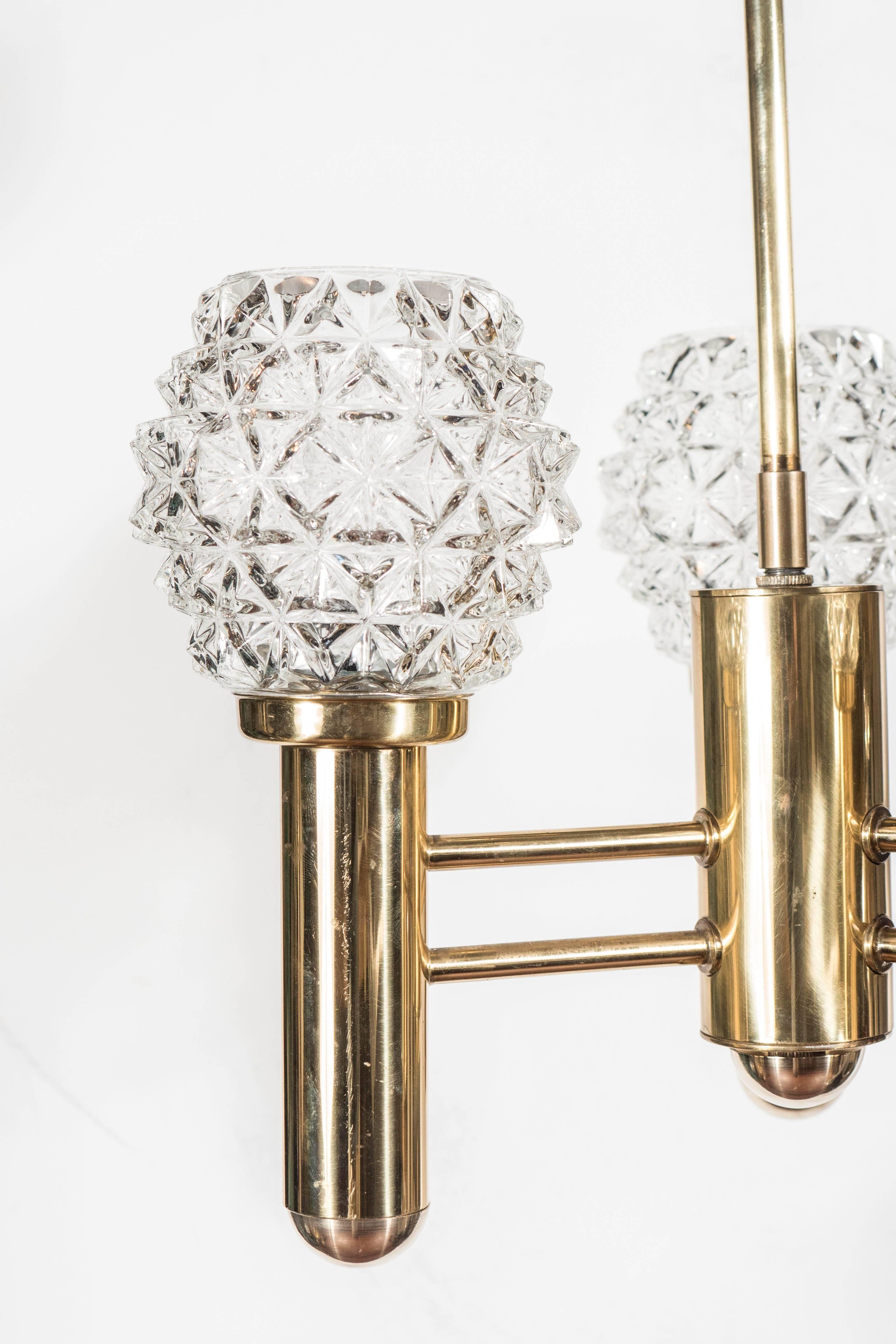 An exquisite Mid-Century Modernist three-arm chandelier in polished brass with multi-faceted crystal shades by Richard Essig. A rounded edge frame complements a set of three sparkling multi-faceted crystal shades. A perfect balance of Mid-Century