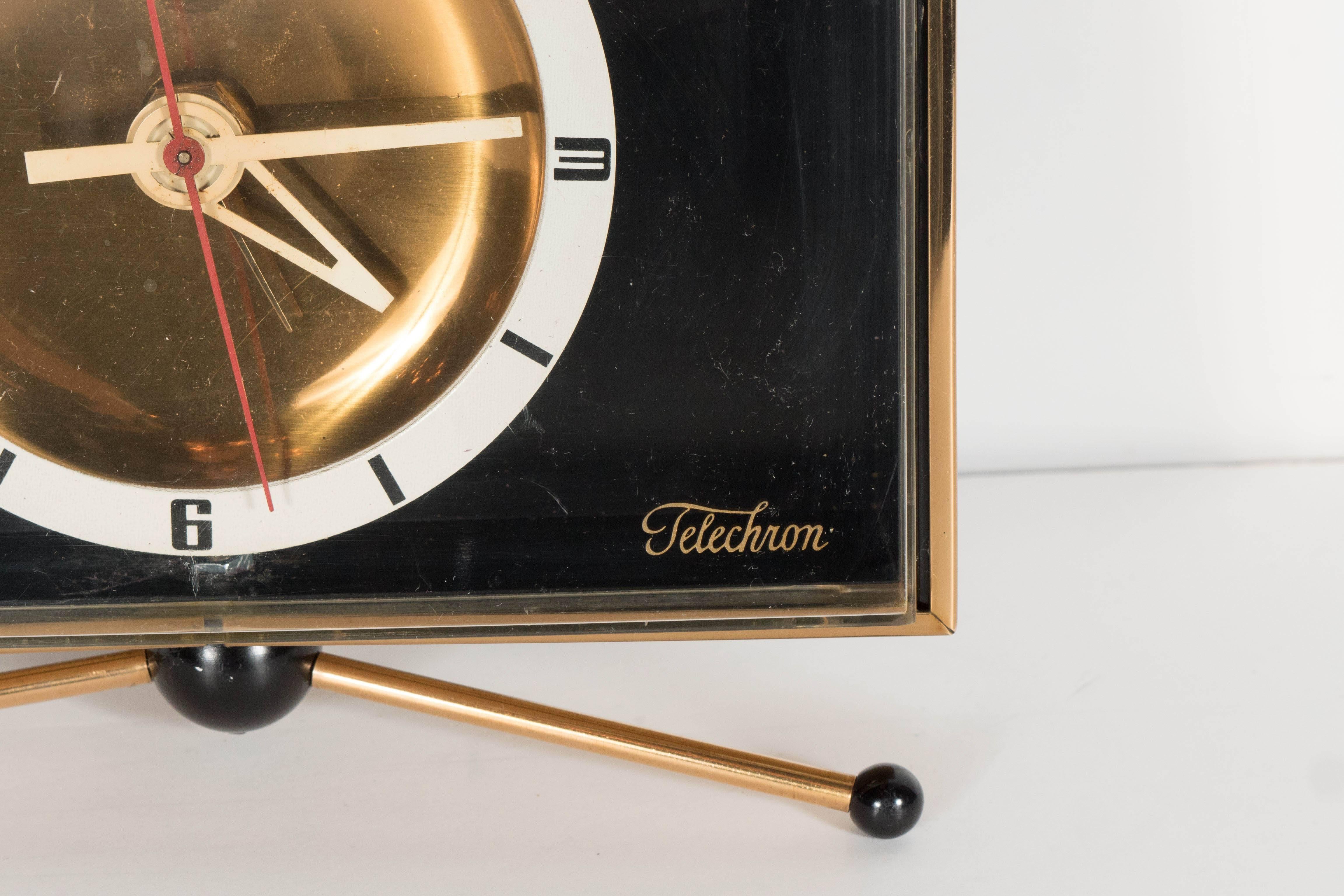 A Classic example of Mid-Century Modernism's clean aesthetic and style. A brass tripod with ball-points holds a fully original Telechron clock resting within a rectangular polished-brass frame. A striking brass dial is surrounded by a red second