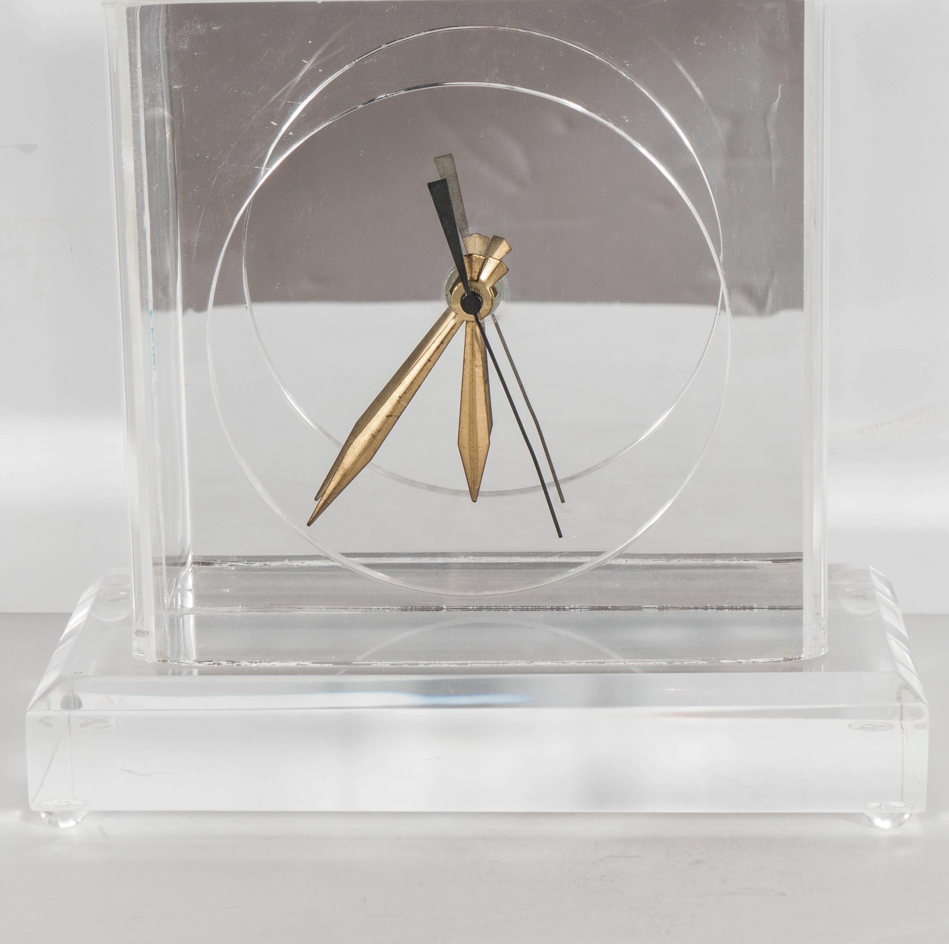 A chic Mid-Century Modernist desk or table clock. A thick-beveled Lucite plinth supports a molded Lucite frame, which holds a mirrored-back clock with brass arms. A simple and elegant design. This piece is in excellent condition.