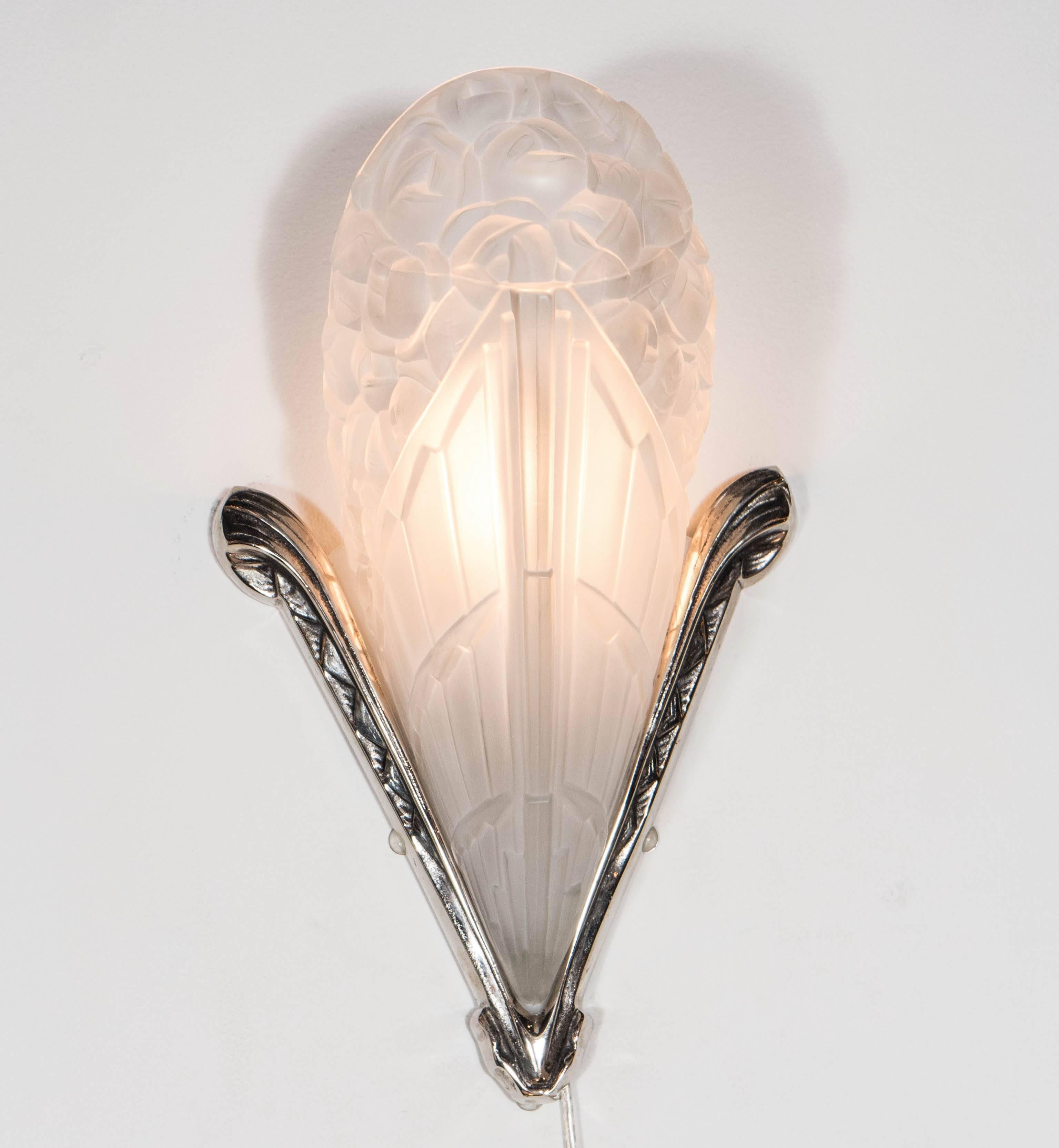 This gorgeous pair of French Art Deco sconces by Degue feature a polished nickel V-Form frame with leaf like fronds at the ends and a lineal etching that runs along each arm of the frame, the frosted glass shade is a motif depicting bouquet of