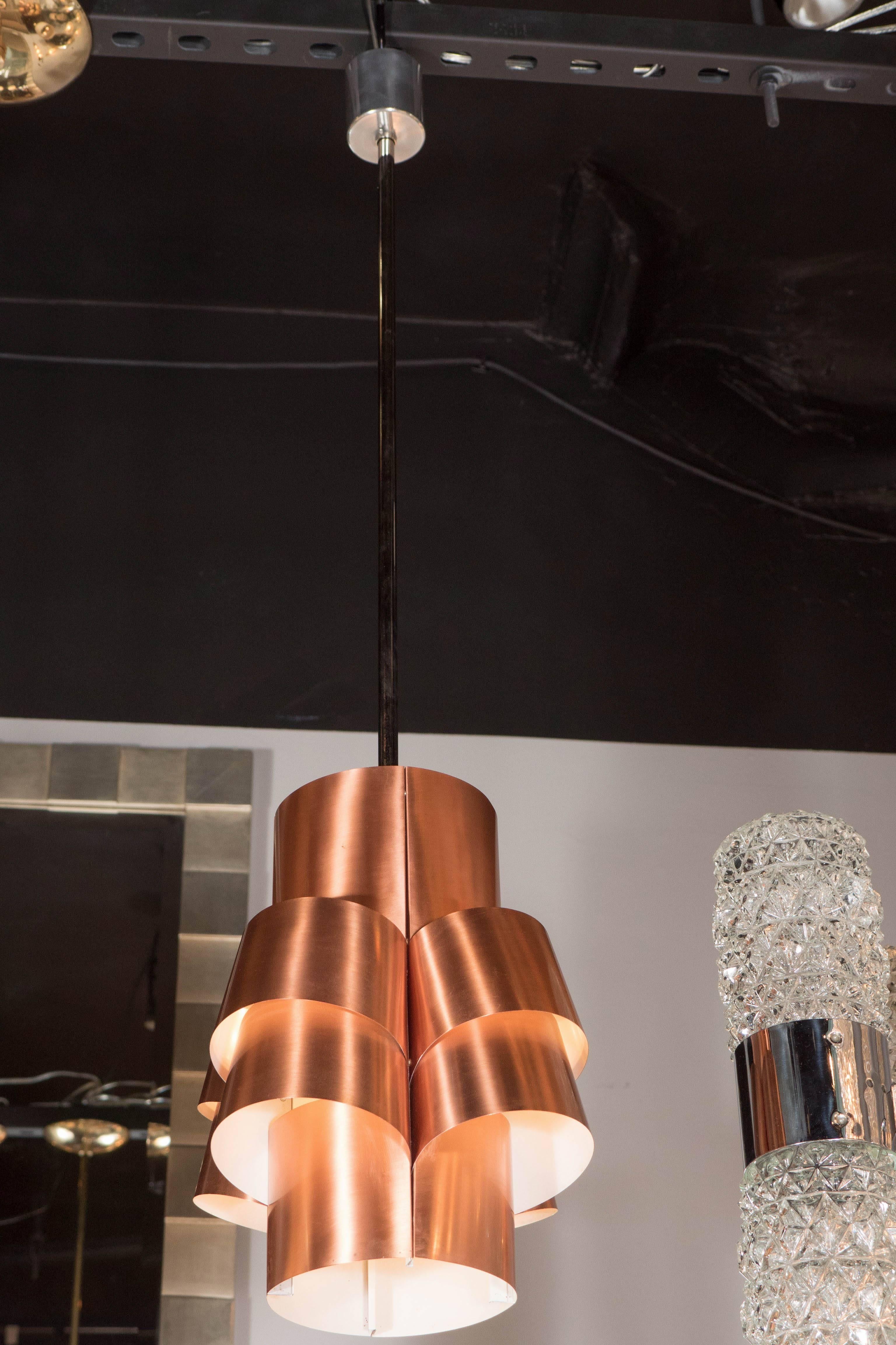 Una splendida lampada a sospensione a segmenti del Mid-Century Modernist in rame spazzolato di Hans-Agne Jakobsson. Segmenti di rame spazzolato ornano un design tubolare sospeso verticalmente, con un interno bianco. Questo pezzo è tipico