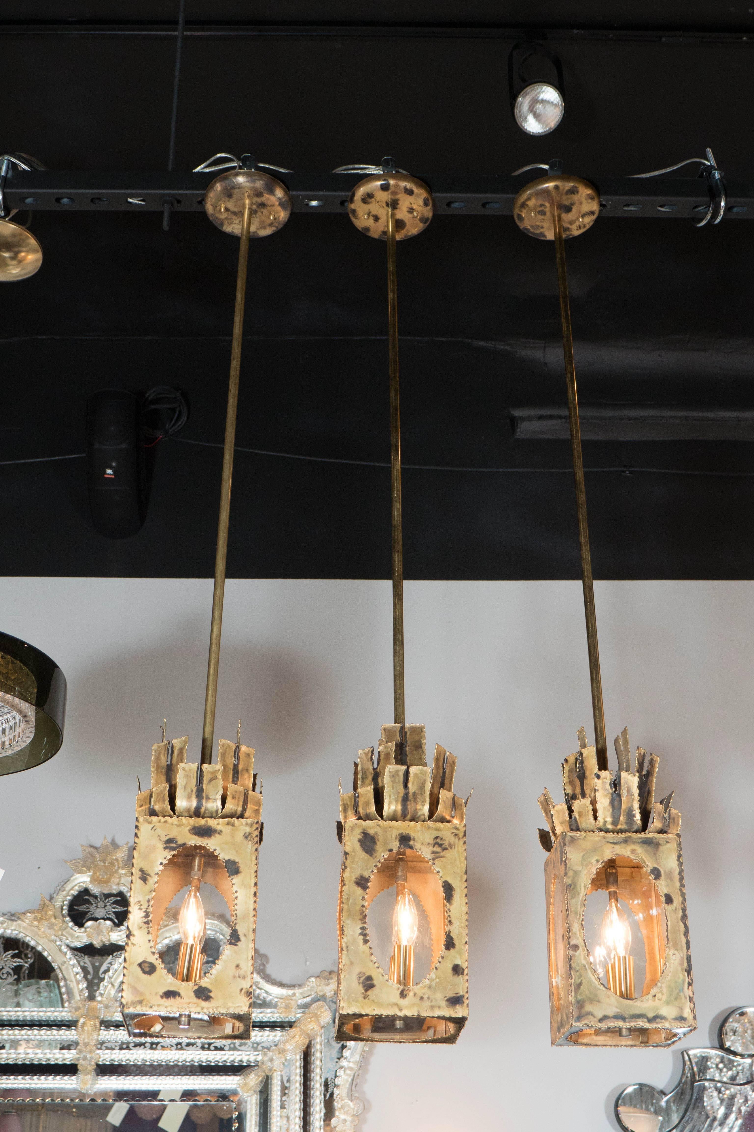 A terrific Mid-Century Modernist Brutalist pendant by Tom Greene featuring torch-cut patinated brass box frame that holds a single bulb. Its top offers sculptural segments mimicking stylized lanterns, or flames. A really exquisite burnt effect from