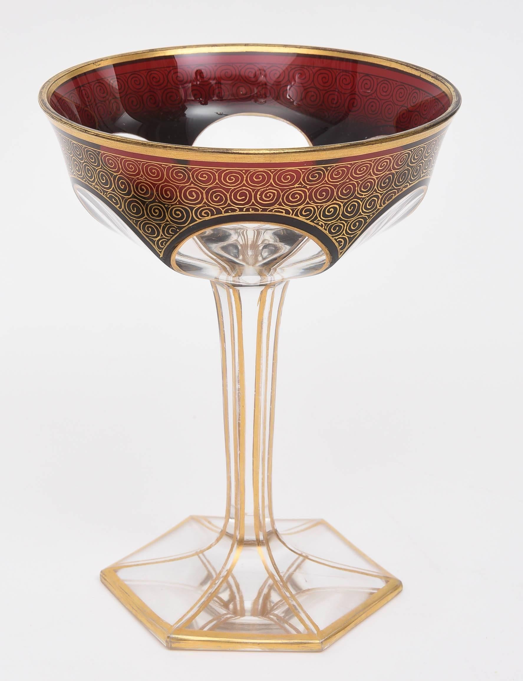 A scarce and hard to find service attributed to Moser, last quarter 19th century. A rich dark ruby cased and cut to clear design with shaped bases, elongated stems and petal form patterns. Swirls of hand gilt gold on the rich jewel colored ground as