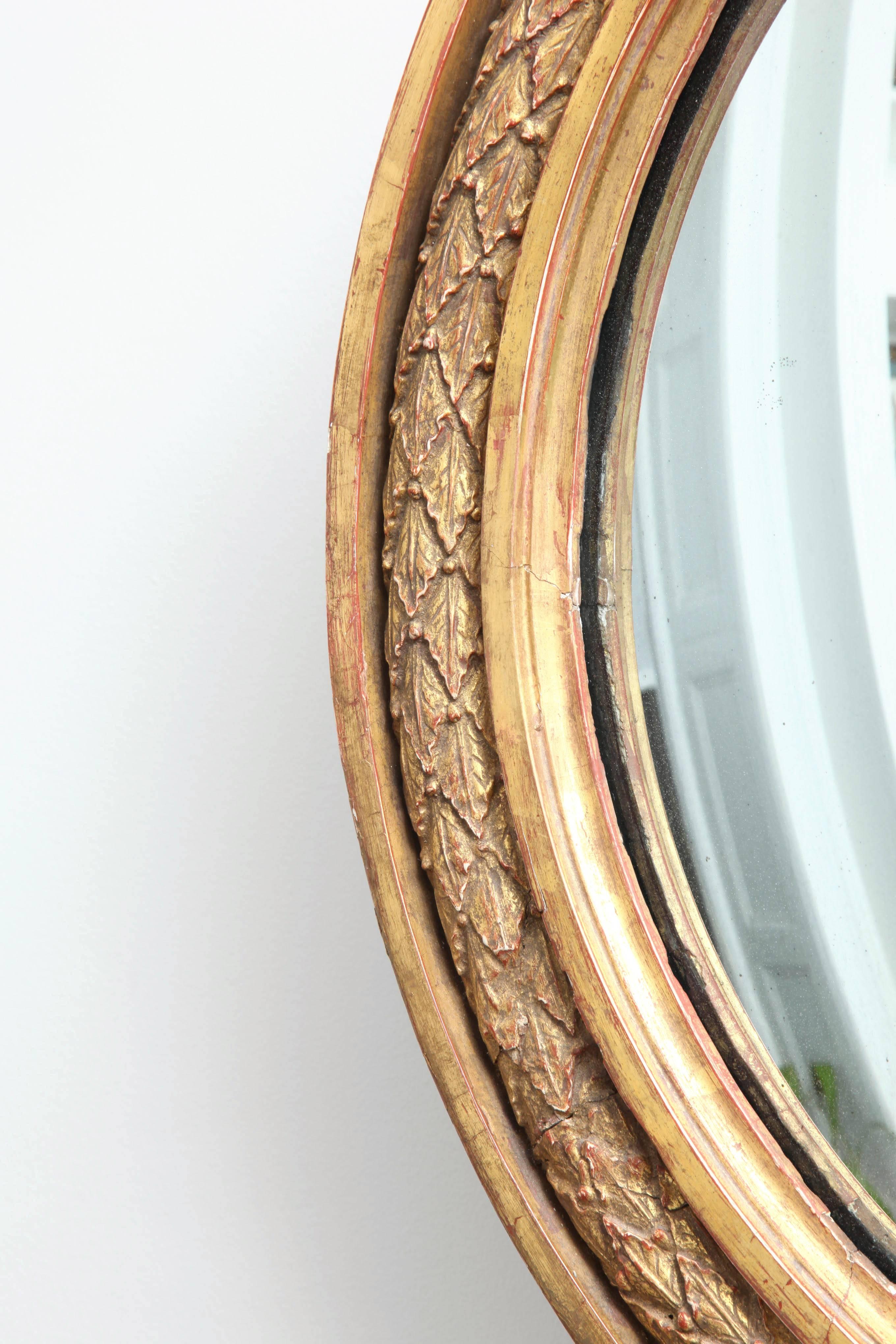 An English Regency carved giltwood convex mirror with moulded edge enclosing leaf-tip carved banding and original mercury glass plate.