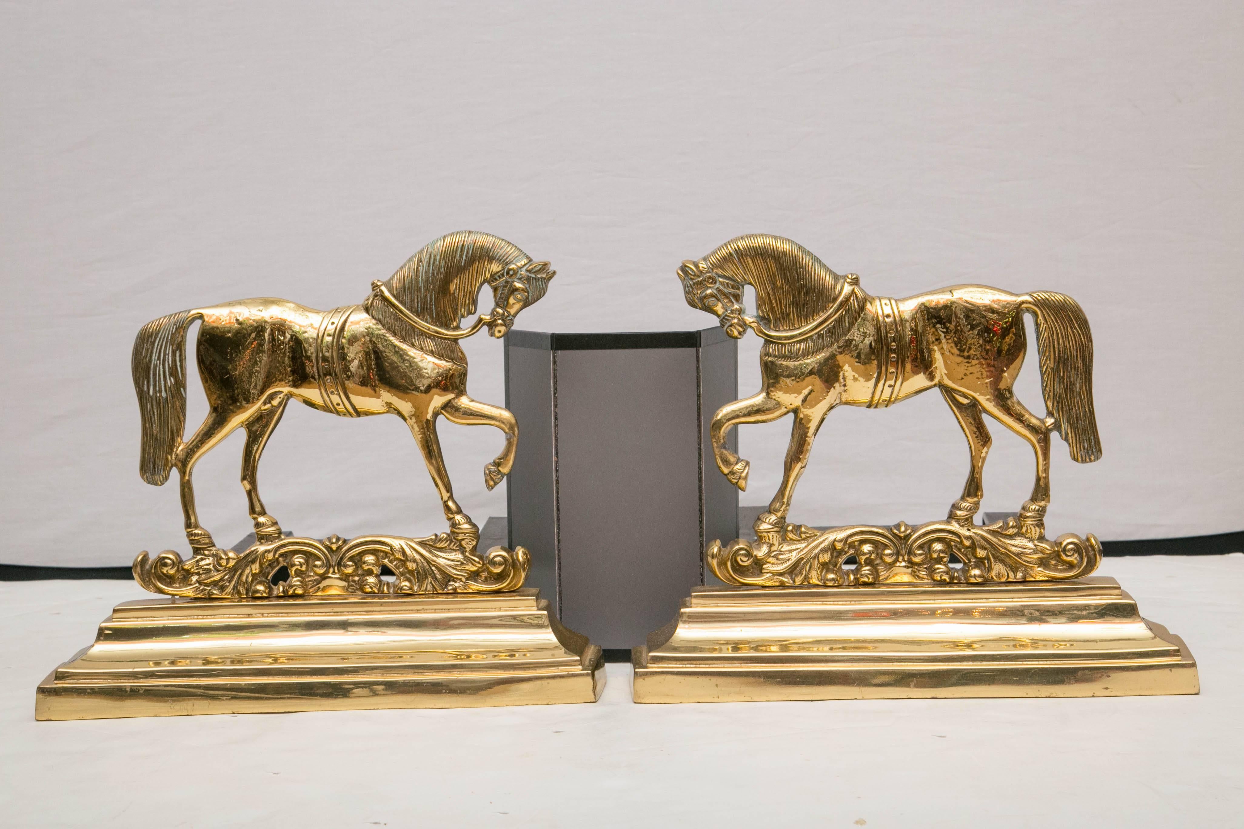 Ein spiegelbildliches Paar Pferdefiguren aus Messing auf dekorativen Sockeln, die an schwarzen Eisenstützen befestigt sind.