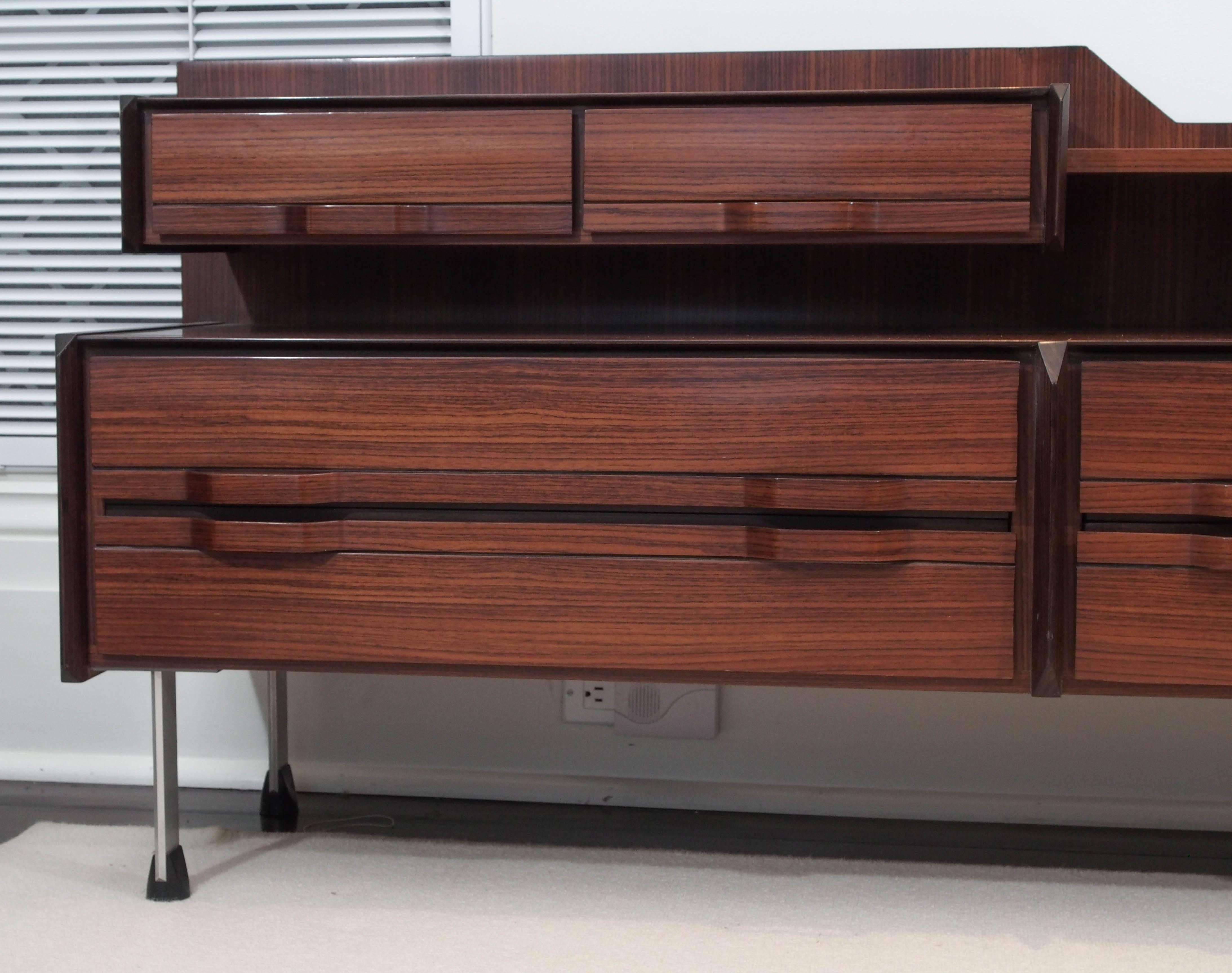Two level credenza in teak; two drawers above, four below, each with shaped integral pulls; steel legs with rubber feet.