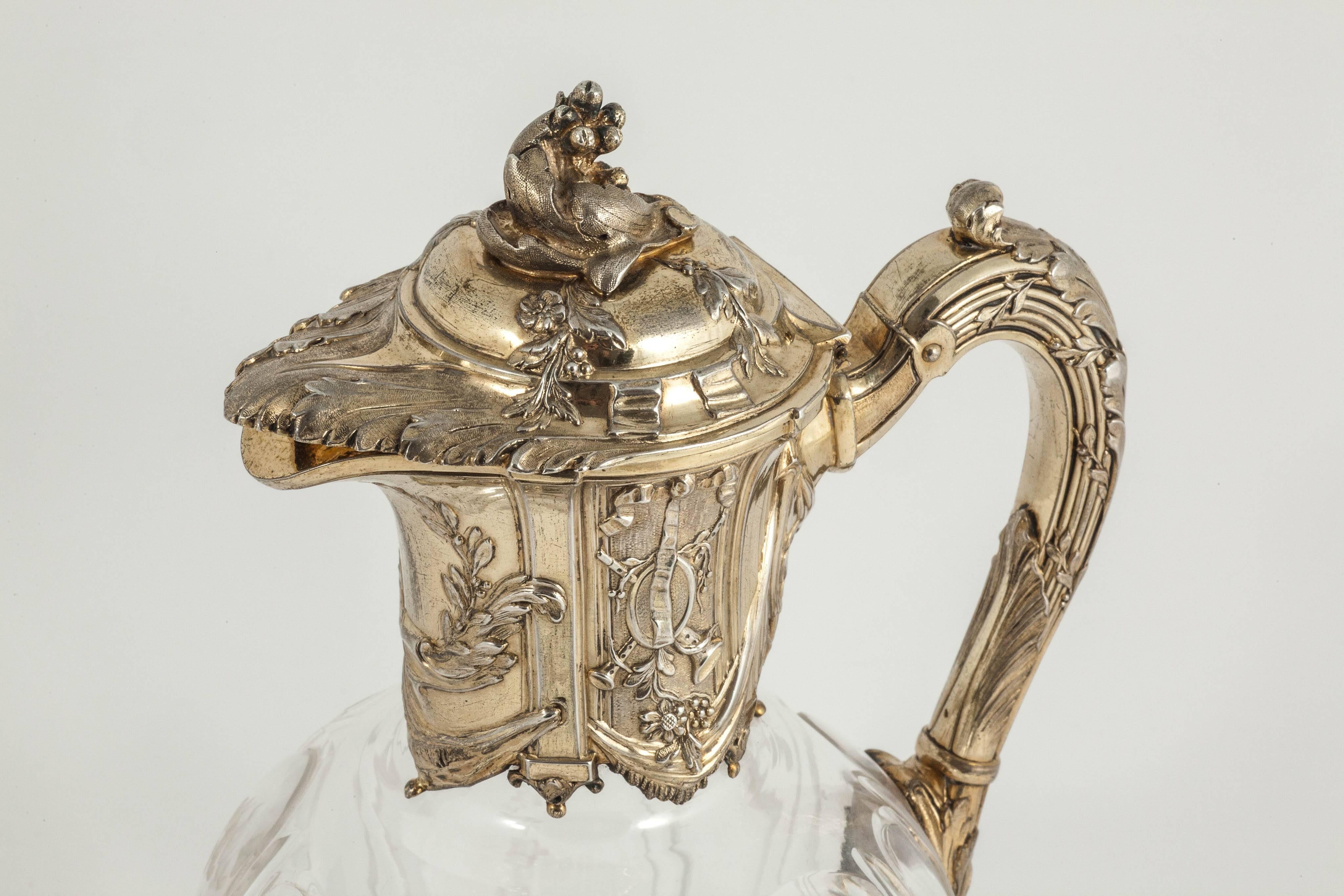 A lovely English hand-cut crystal claret jug or wine jug with gold-plated sterling silver mounts in the French style.The silver-gilt collar is decorated with panels on both sides, one showing musical instruments and the other depicting gardening