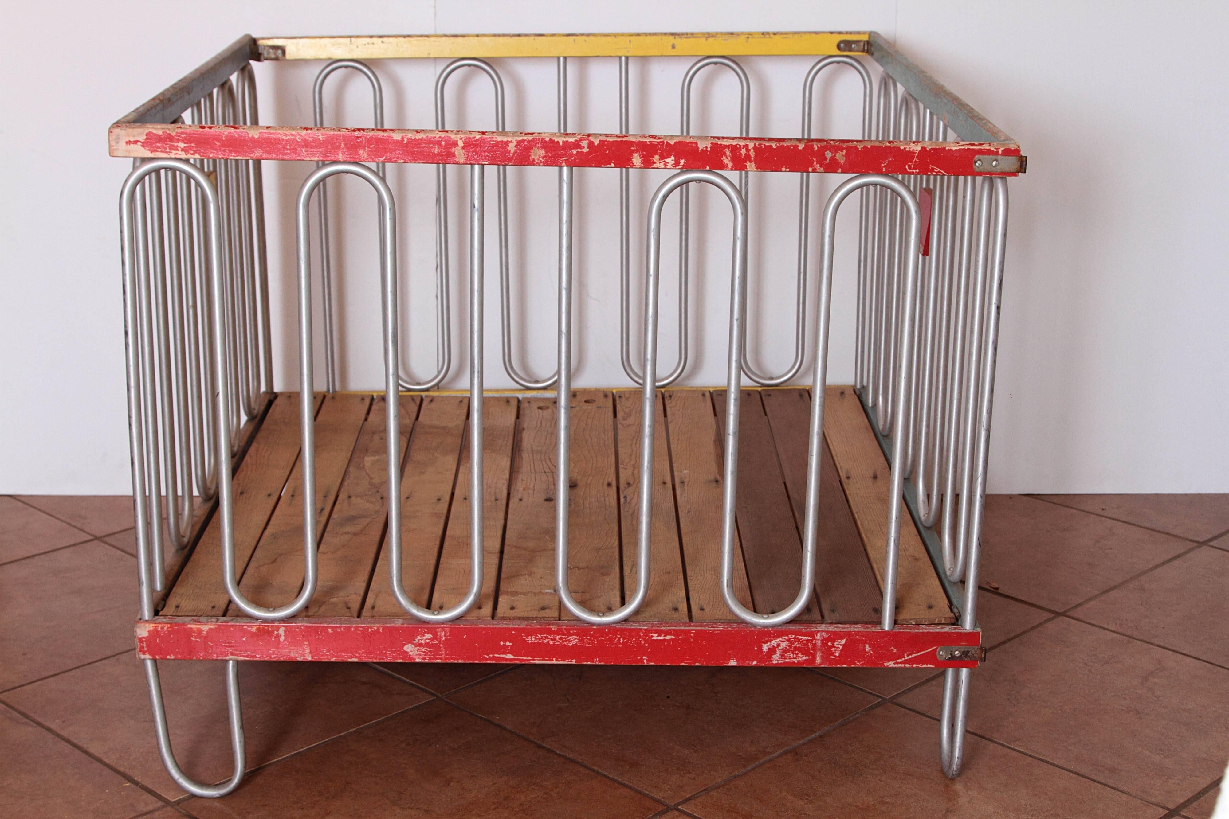 Streamline modernist Art Deco playpen or crib after Gilbert Rohde

Multi-color wooden frame with brushed aluminum tubing sides/feet.
Hinged and latched, fully collapsible to just 4