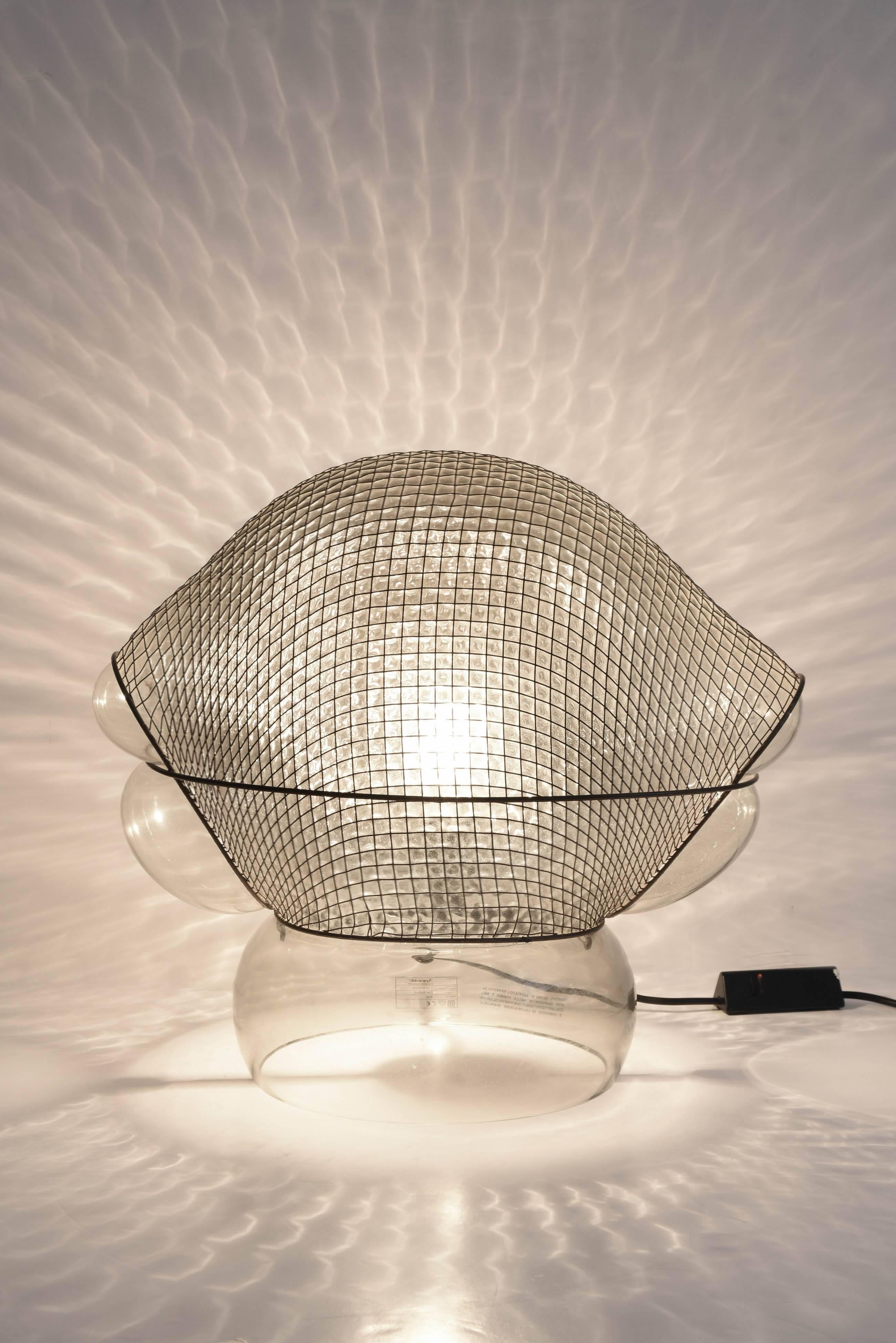 Table lamp by Gae Aulenti “Patroclo” produced by Artemide 1975. With dimmer. Body in transparent blown glass with armor in steel wires.Labeled: Artemide
modern classic 
PATROCLO
Gae Aulenti
Italy