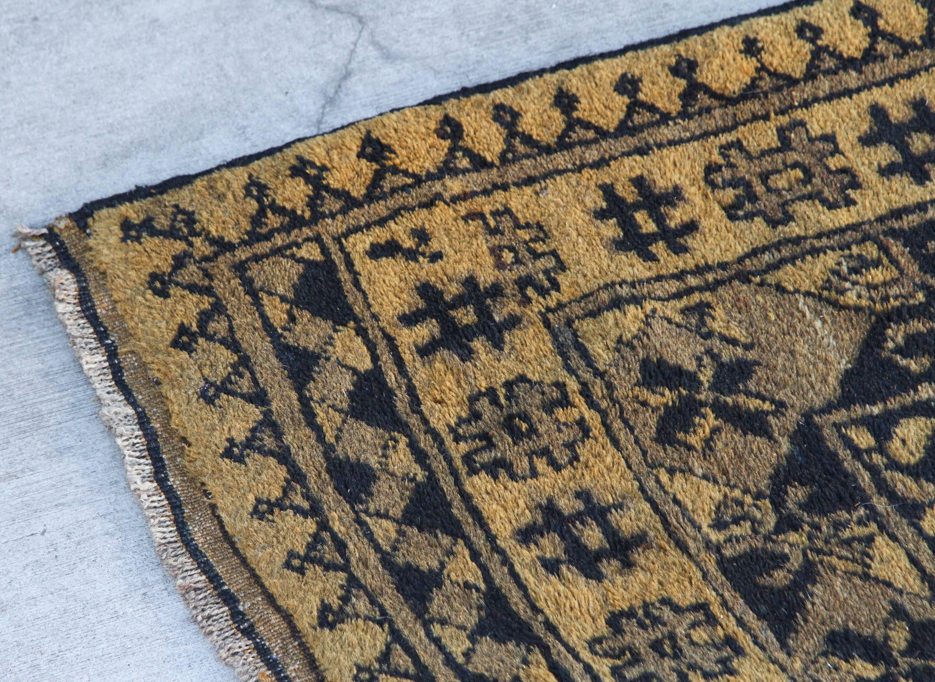 Camel colored Afghan rug with black tribal print. Afghan rugs are handwoven floor-covering textile traditionally made in Afghanistan.