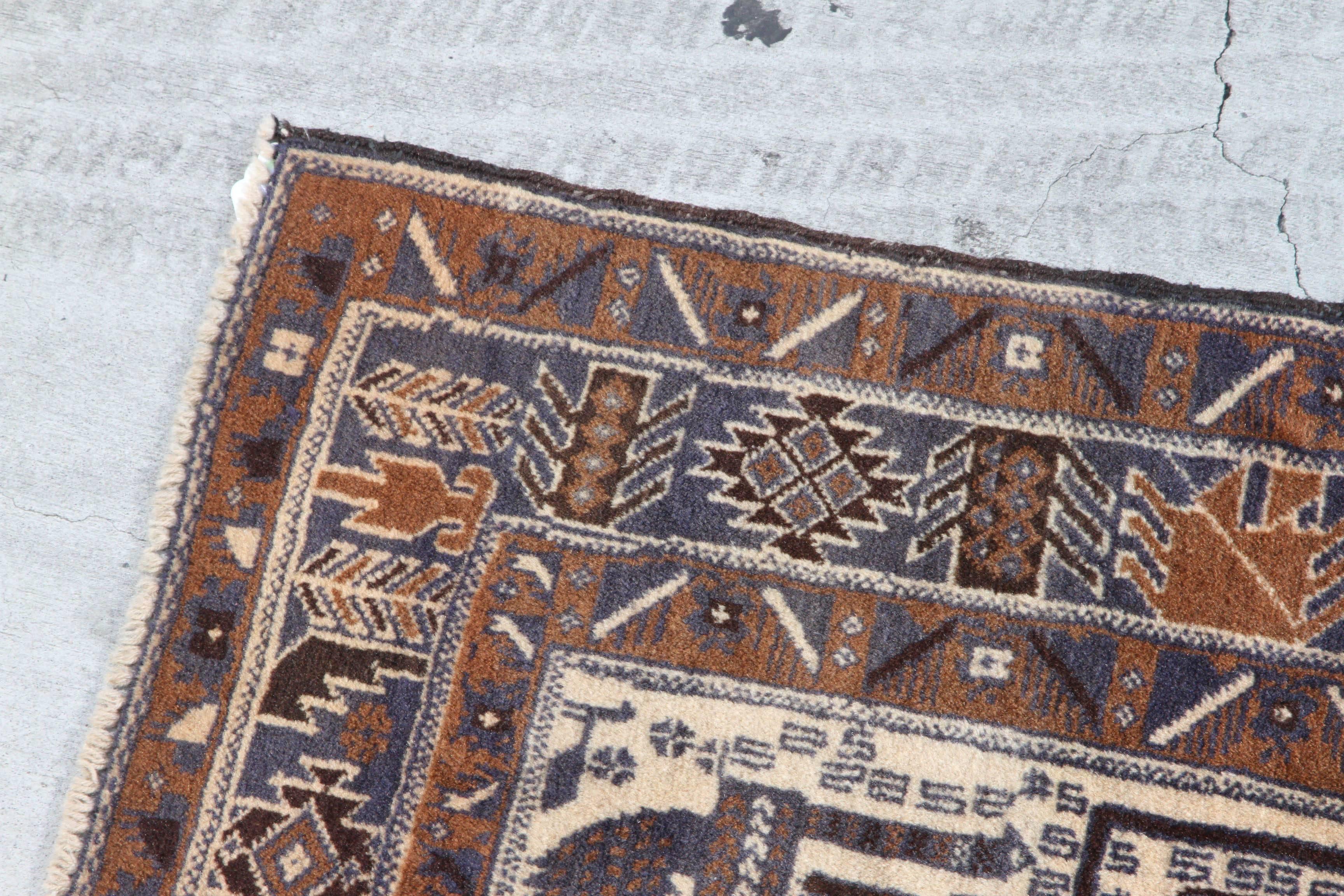 Antique Persian Baluchi rug with blue creatures and warm hues pattern surrounding them. Baluchi carpets are handmade carpets originally made by Baluch nomads, living near Iraq, Pakistan and Afghanistan.