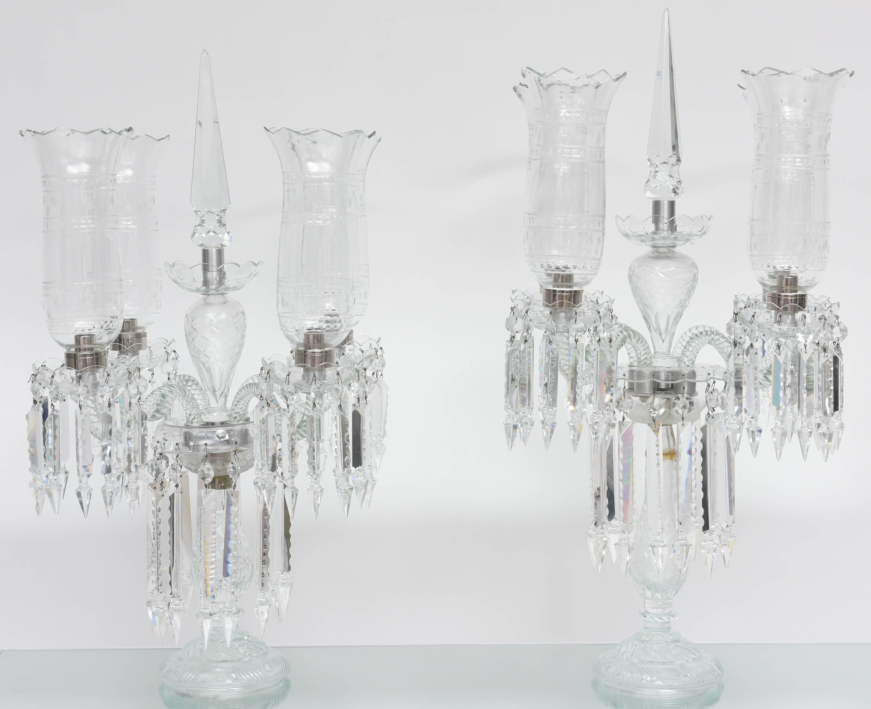 This monumental pair of Baccarat attrubuted Regency style girandoles date from the late 19th to early 20th century. They are hand-cut crystal with four candle-arms with hurricanes globes.  At some point the central support stems were damaged and