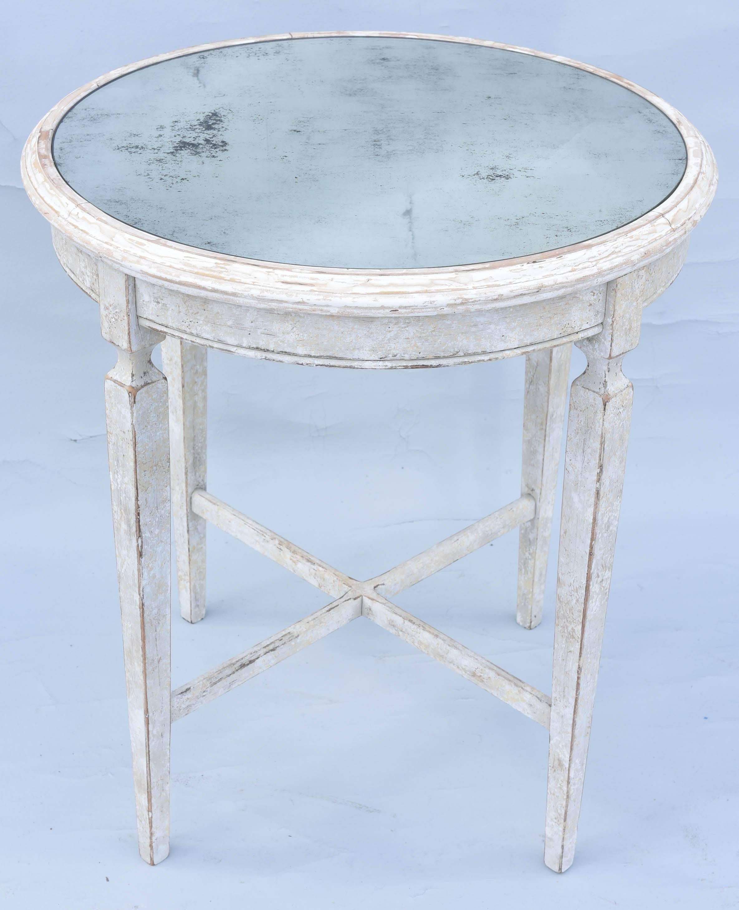 Swedish style occasional, or end table, having a round top of distressed mirror, inset on painted table base, showing natural wear, its fielded apron, raised on four, square-section, tapering legs, joined by X-stretcher. 

Stock ID: D2514.