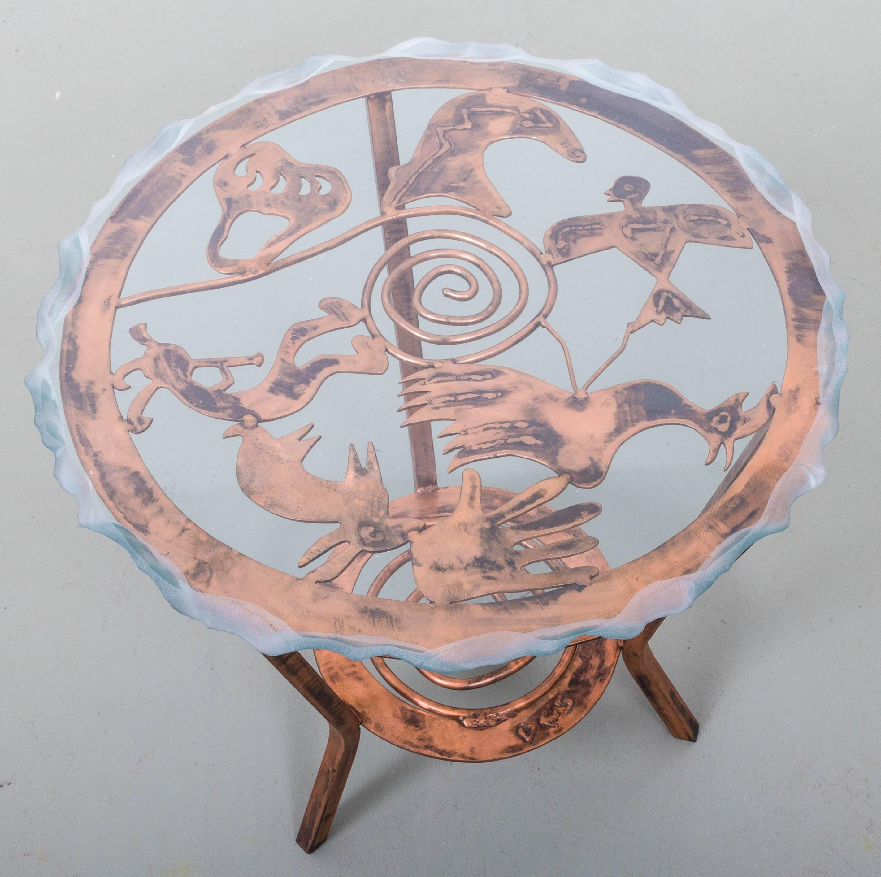Copper three-leg two-tier table with spiral design and stylized Native American motifs, bear paw, eagle, dancing musician, phoenix bird, rabbit and bear. Fire finished glass top.