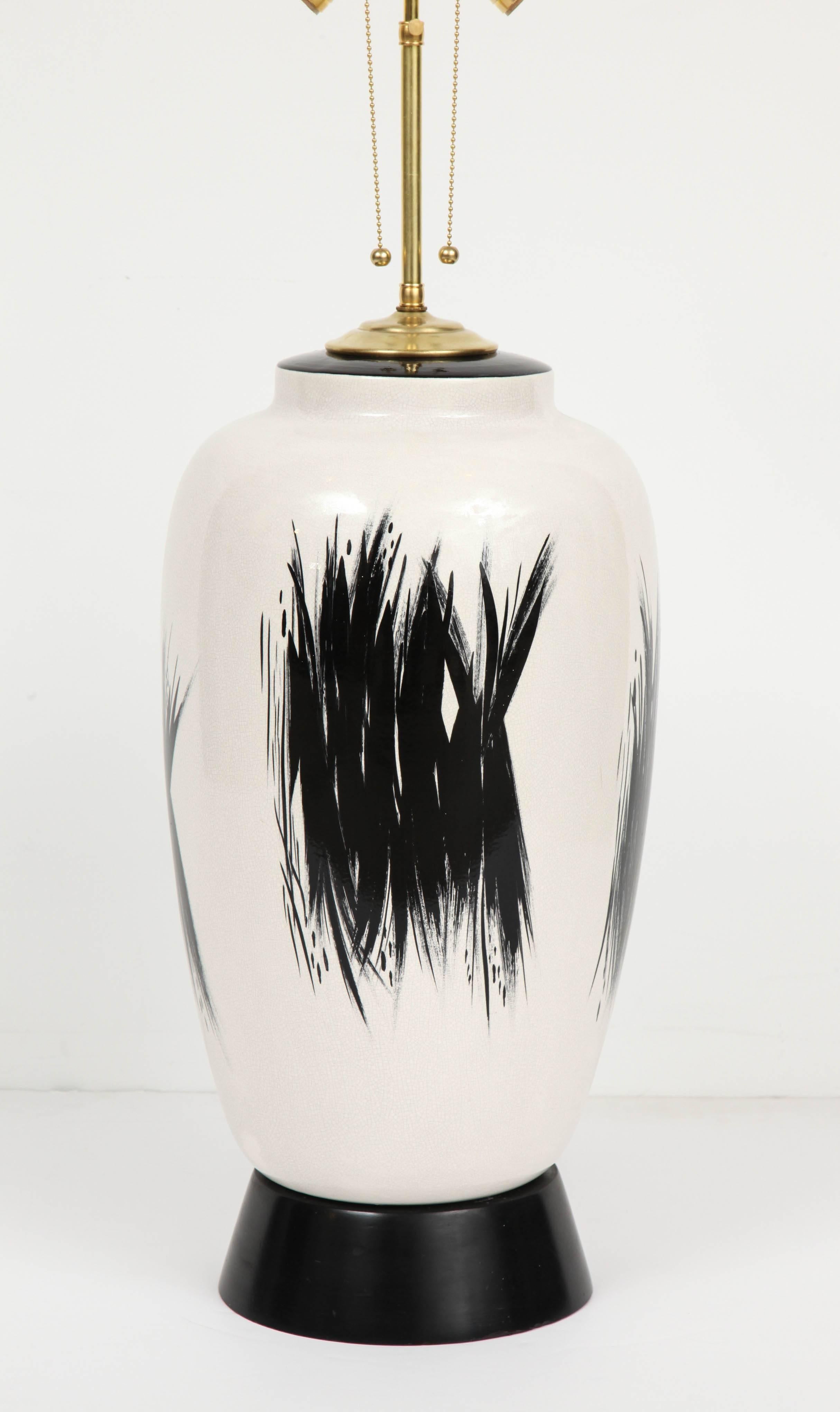 Elongated ovoid body in soft white crackled ceramic hand-painted with angular black brush-stroke design, mounted on original thick black painted wooden base. Newly rewired and refitted with two-socket cluster, Japan, early 1950s. Lamp base and body