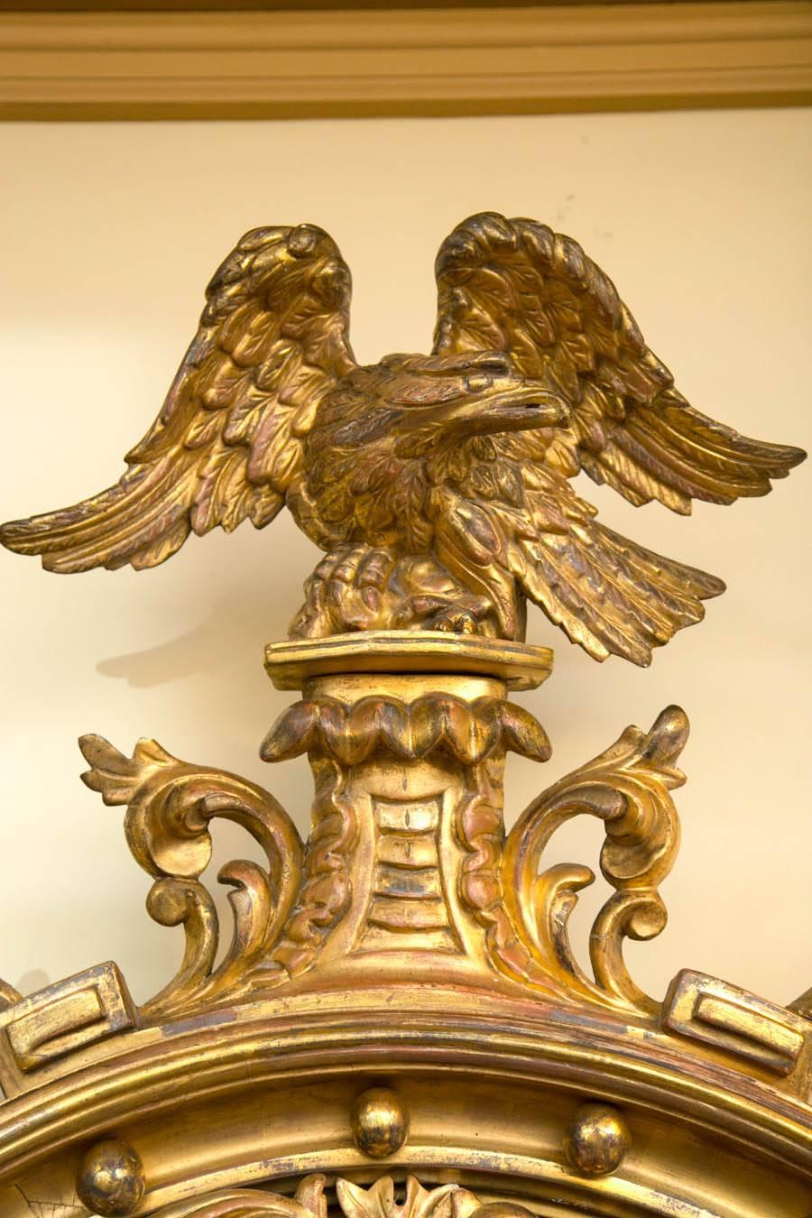Early 19th century gilt-gesso and wood convex mirror, the crest with spread wing eagle perched on a plinth flanked by foliate devices, above the molded frame with applied spherules, a reticulated interior band of scrolling leaves and rosettes, and