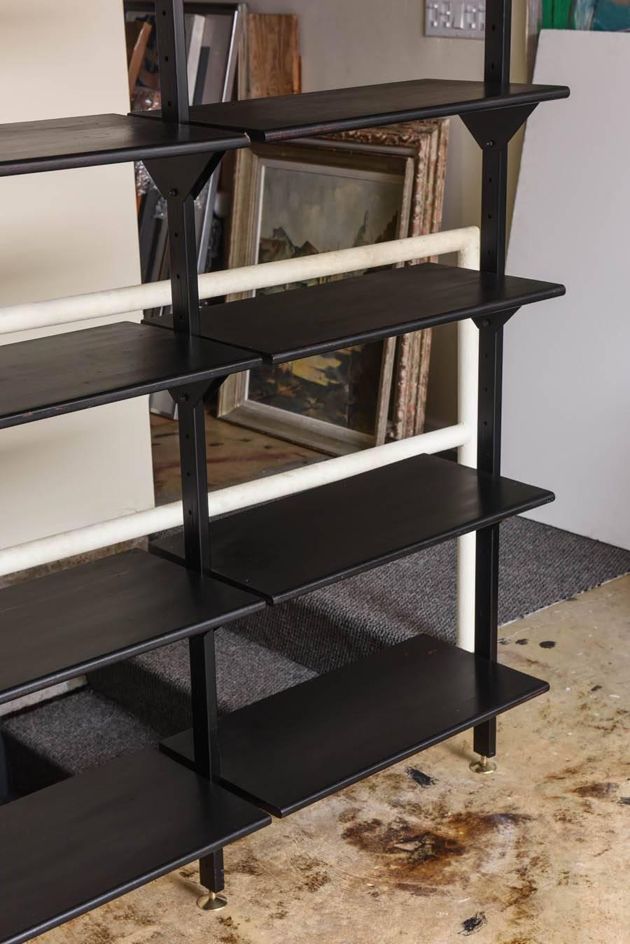 Rare industrial wall-mounted library or shelving system that is completely customize-able to your design needs.  A long shelving unit fitted with five posts in black lacquered metal.  Posts have brass sabot to base that supports the various shelves.