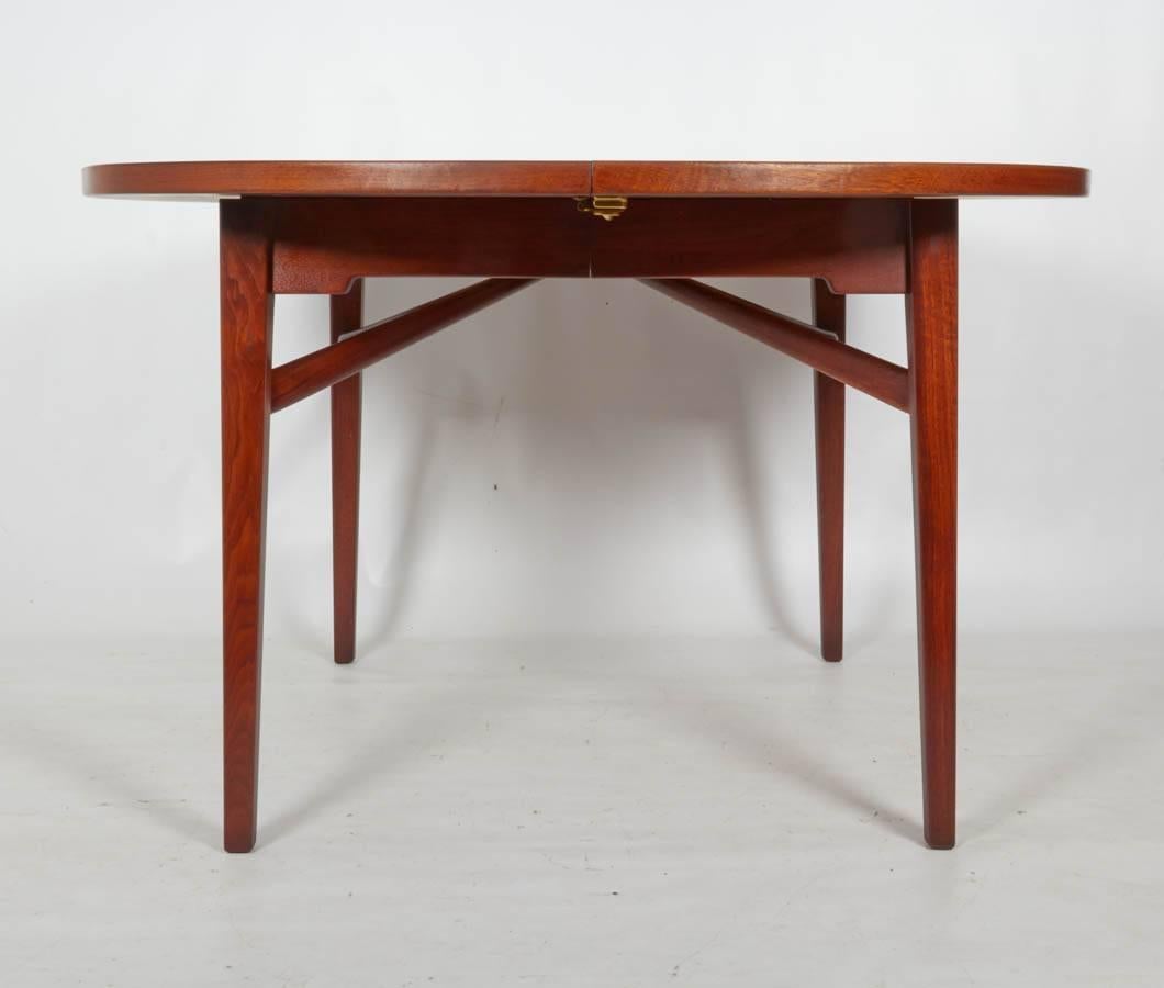 Handsome walnut dining table beautifully designed with Jens Risom's signature details. Please note that when the table is closed it is more of an oval form than a circular one. The table has three extensions and each extension measures 15.75 inches.